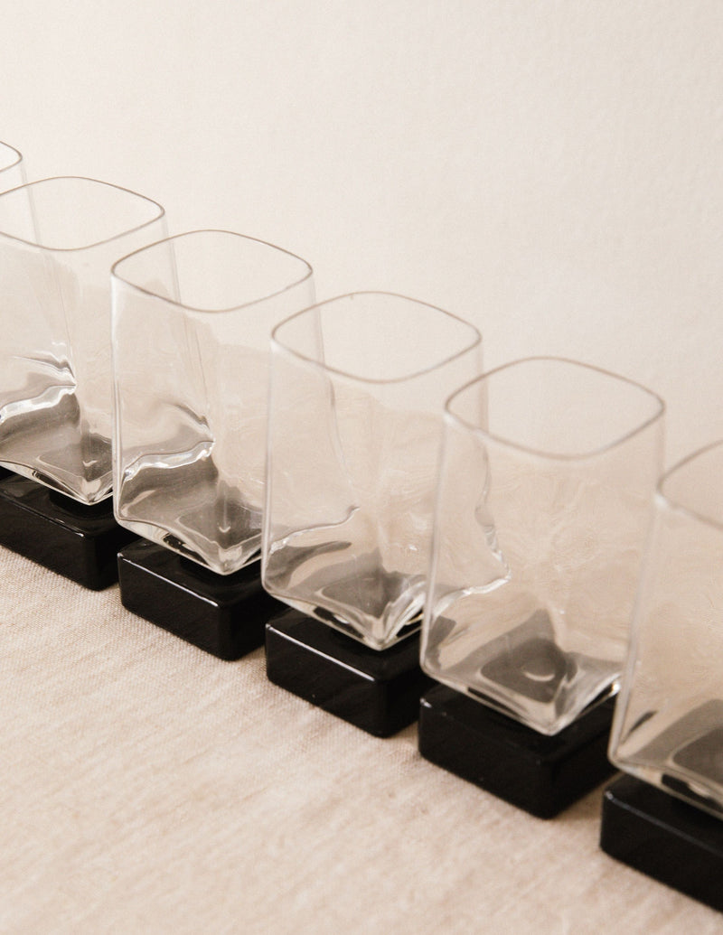 Four clear glass liqueur glasses arranged on black square bases