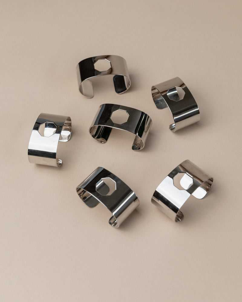 Polished silver napkin rings arranged on beige surface showing reflective finish