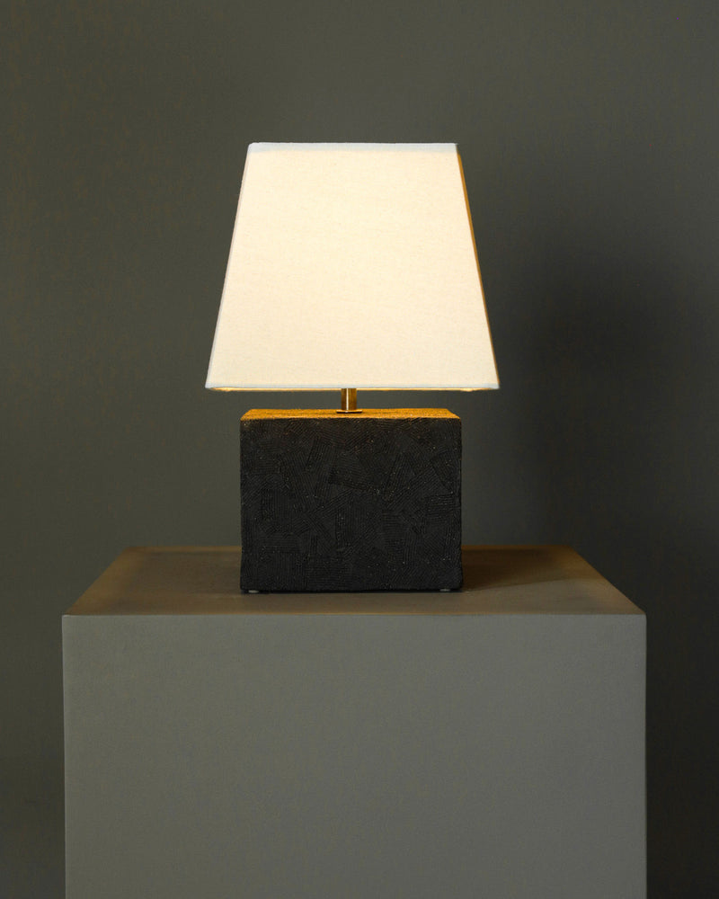 The Akune Ceramic Lamp - Number Four by Studio OSKLO features a white square shade and dark rectangular base, resting on a gray pedestal and evoking post-Bauhaus brutalism against a neutral gray backdrop.