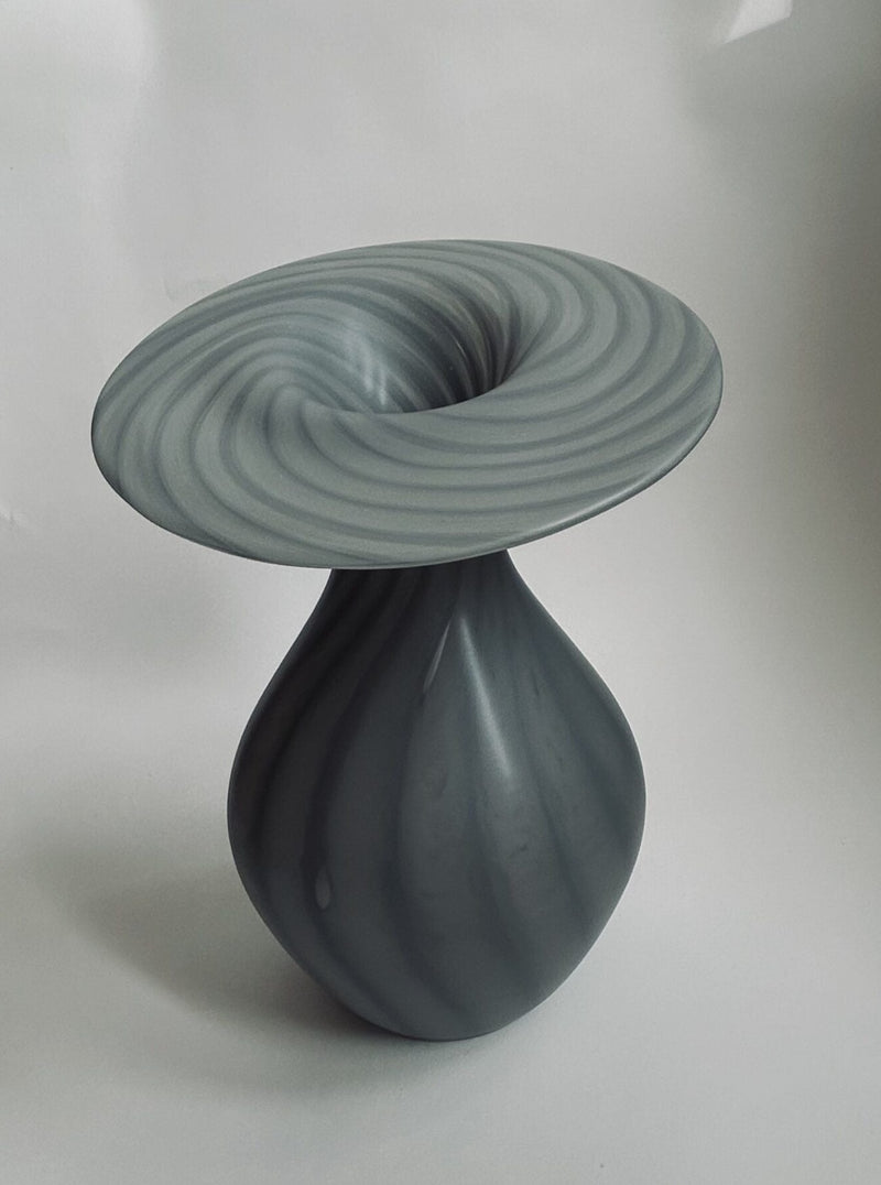 A vase-shaped sculpture with a swirling design by Flock Studio, crafted from high-quality glass, showcases a ribbed pattern and a wide spiraled top. It features smooth, shiny gray tones reminiscent of the Vintage Vase Peill & Putzler against a plain background.