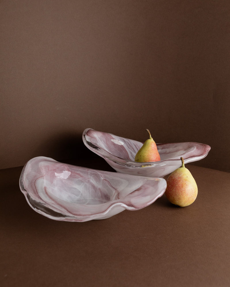 Two pink Murano Glass Bowls by Bottega Jacobs (Italy, 1970s) with white marbling sit on a brown surface beside two yellow-red pears, one inside a bowl and one outside, set against a matching brown backdrop.