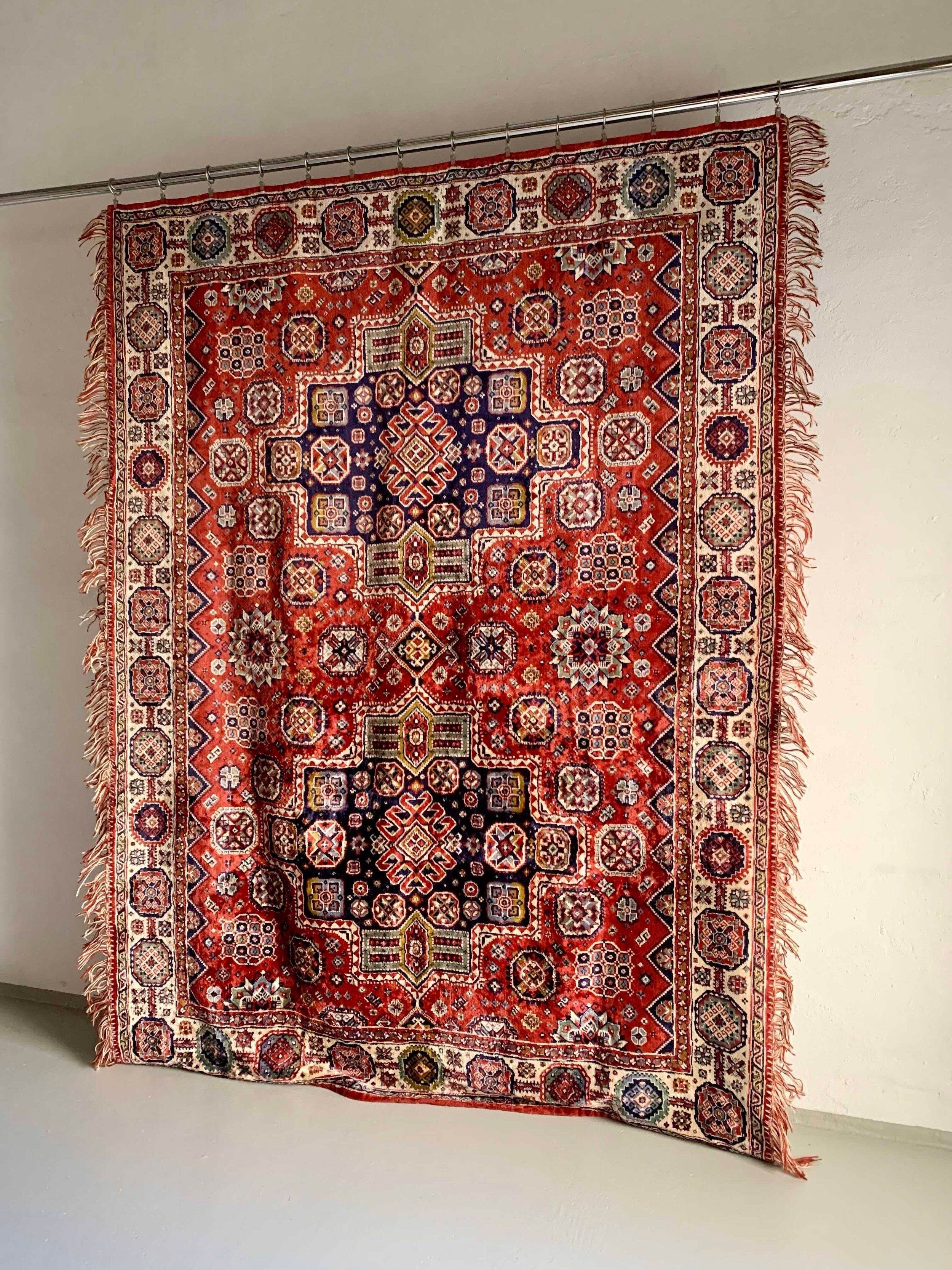 The Veter Vintage "Vintage Silk Oriental Duvet Cover - Rug" features intricate red, blue, and white geometric and floral patterns with fringed edges, displayed vertically against a plain white wall.