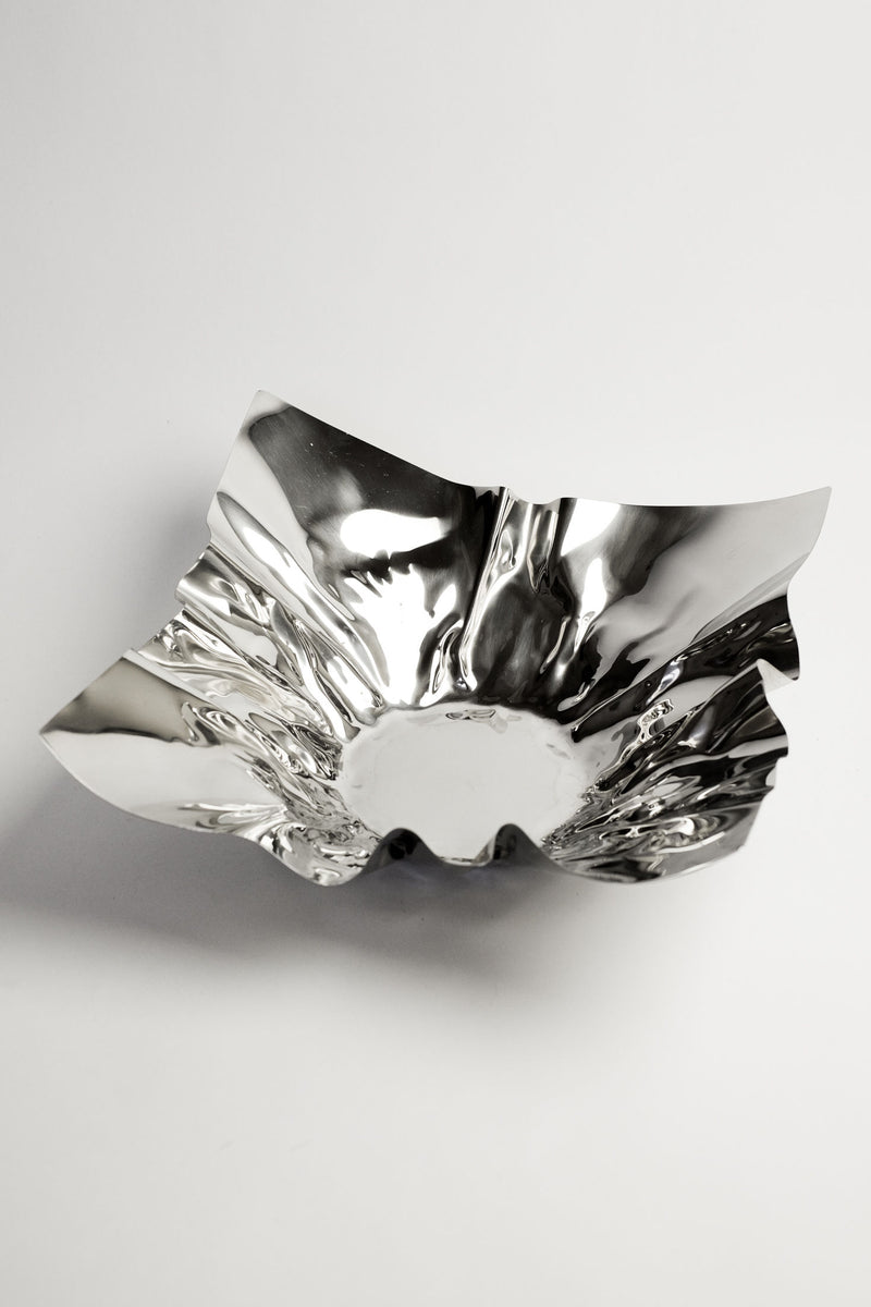 The Extra Large Folded Chrome Bowl by septembre studios features a shiny, vintage-inspired metal design with wavy, irregular edges. Its reflective surface creates striking highlights, bringing unique charm to any interior setting.