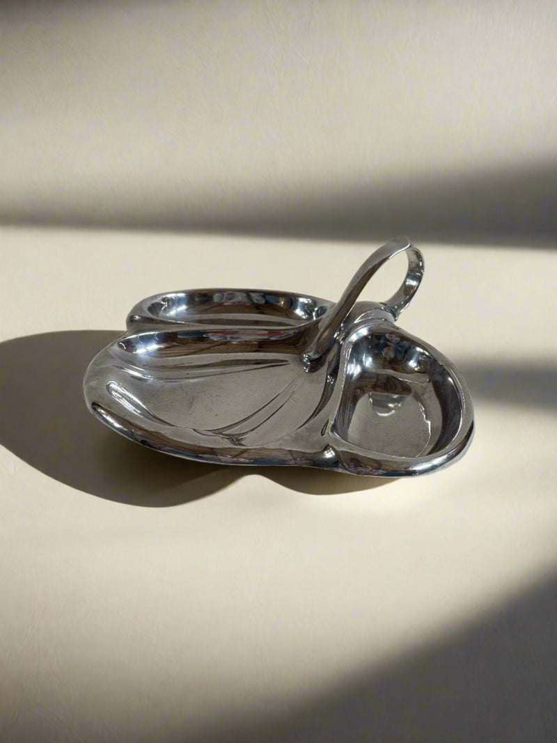A sleek, modernistic silver Maud Vaughan Vintage Mappin and Webb Silver Plate Serving Dish featuring a three-part design. This smart serving dish has a central, slightly elevated handle for easy carrying, and its three separate compartments are rounded and shiny, reflecting light. The background is plain and light-colored.