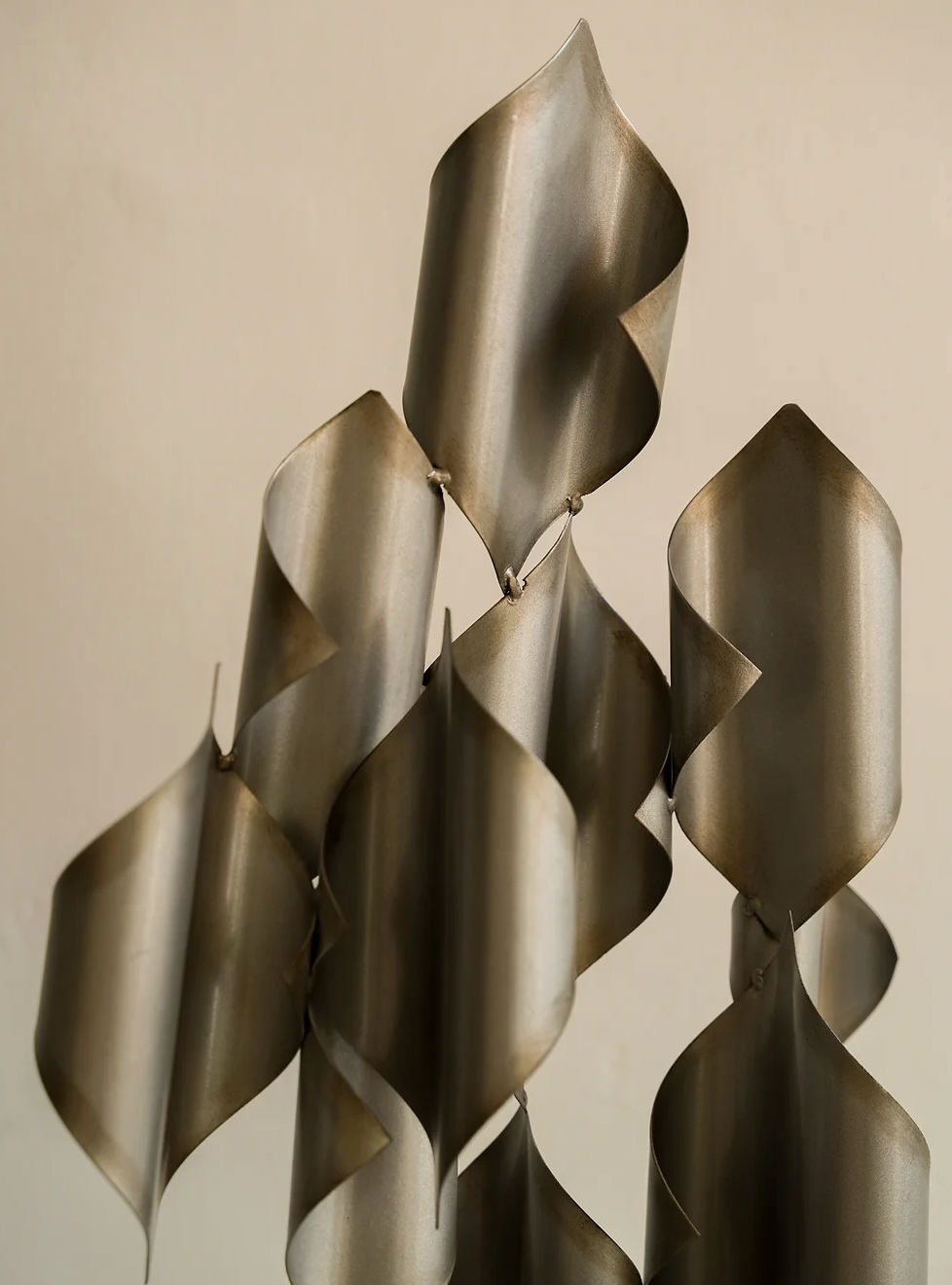 A detailed close-up of the Les Objets Amsterdam Metal Sculpture, featuring curving, ribbon-like elements. The sculpture's metallic surface is smooth and reflective, with varying shades and folds that create a sense of movement and fluidity against a neutral background—making it a stunning addition to modern home decor.