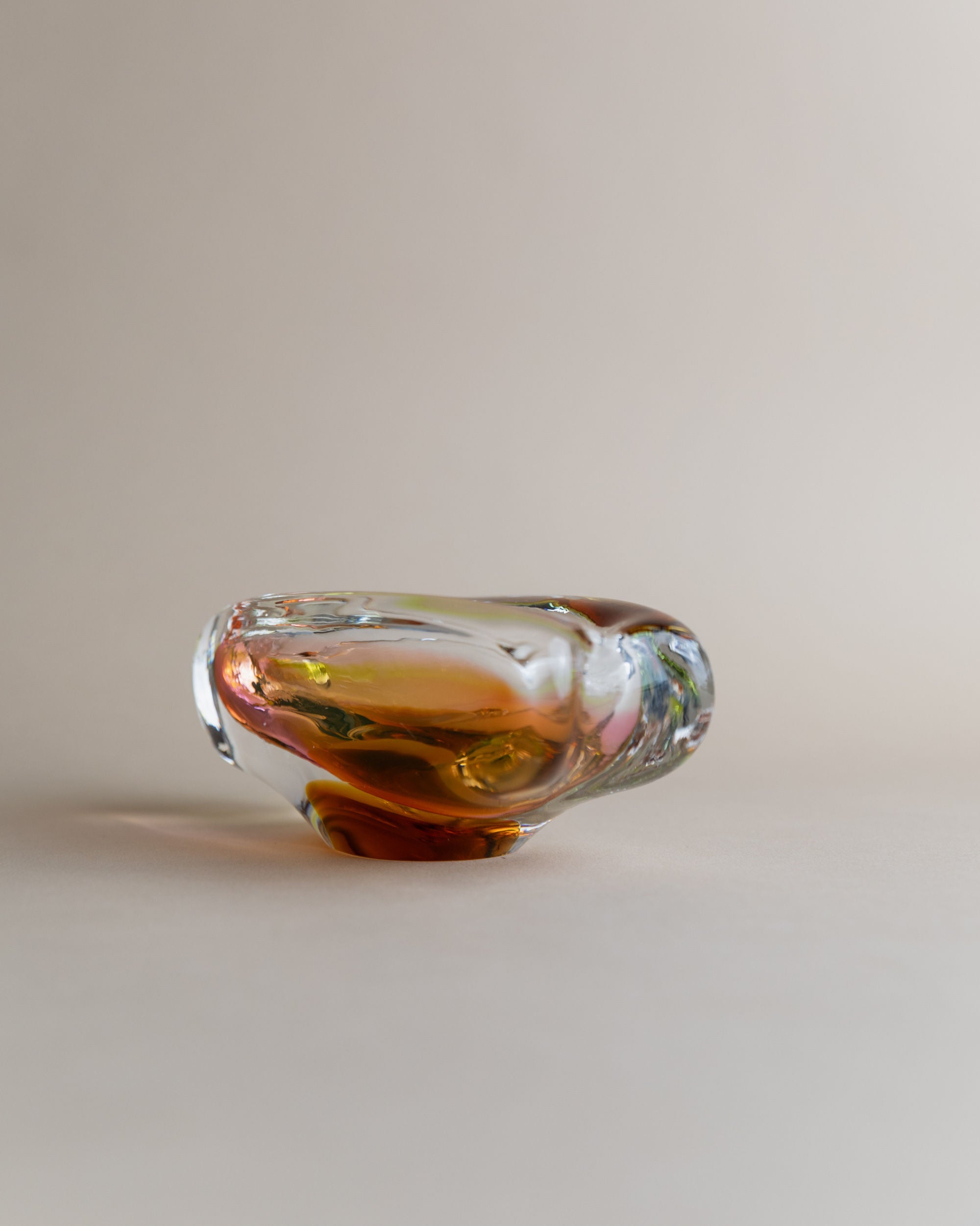 A small abstract sculpture by Josef Rozinek for Novy Bor, the glass ashtray by Bottega Jacobs features swirling amber and brown hues with clear glass accents on a neutral background. Its design echoes Rozinek's aesthetics with an organic, fluid shape and smooth edges.