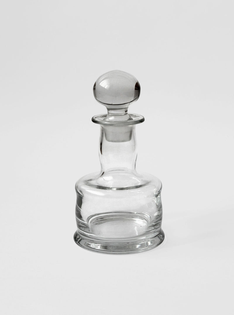 Clear glass mini decanter with rounded stopper, elegant profile view