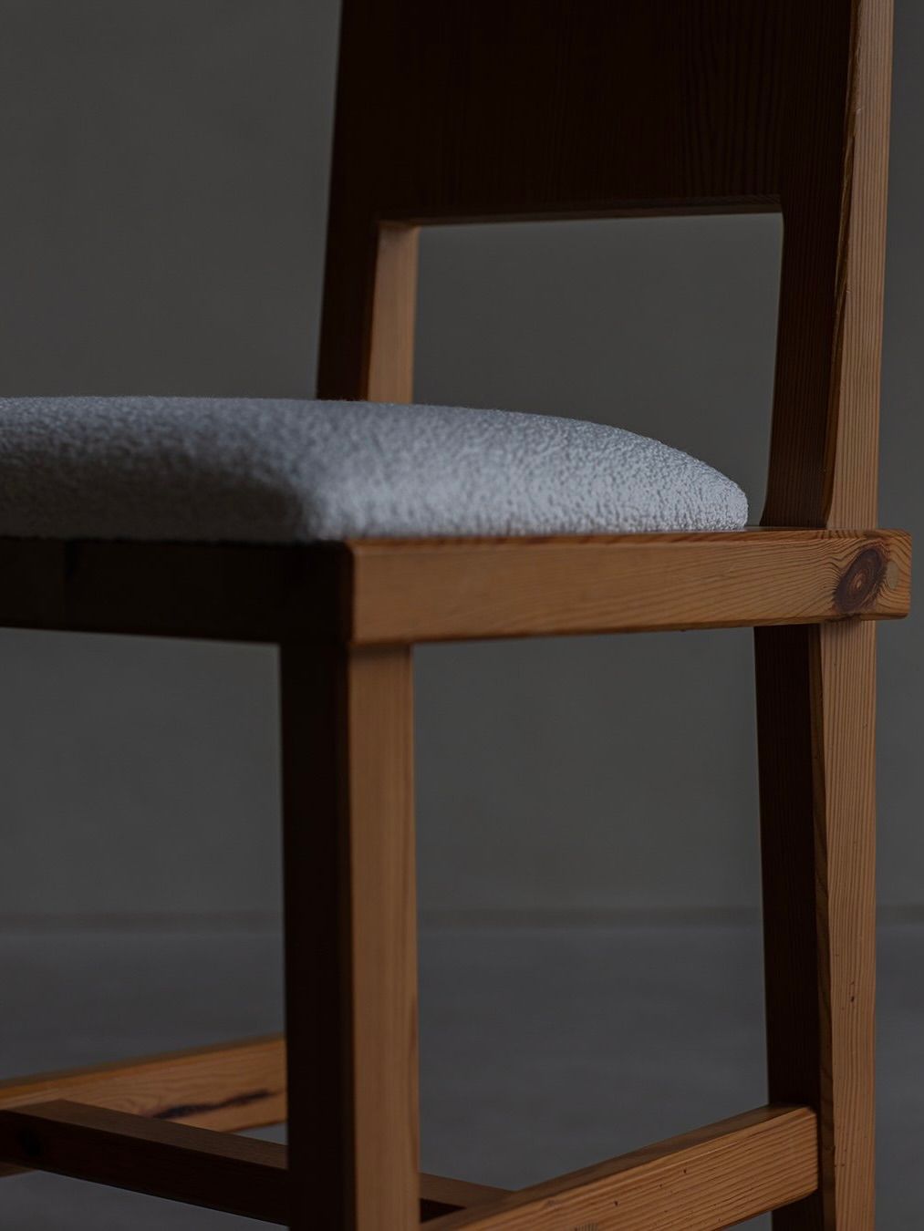 A Göran Malmvall - Model 553 chair from Bicci de' Medici, featuring a wooden square frame and a light gray cushioned seat, is shown against a dark background. Its minimalist design and natural wood texture reflect Swedish elegance reminiscent of classic Göran Malmvall chairs.