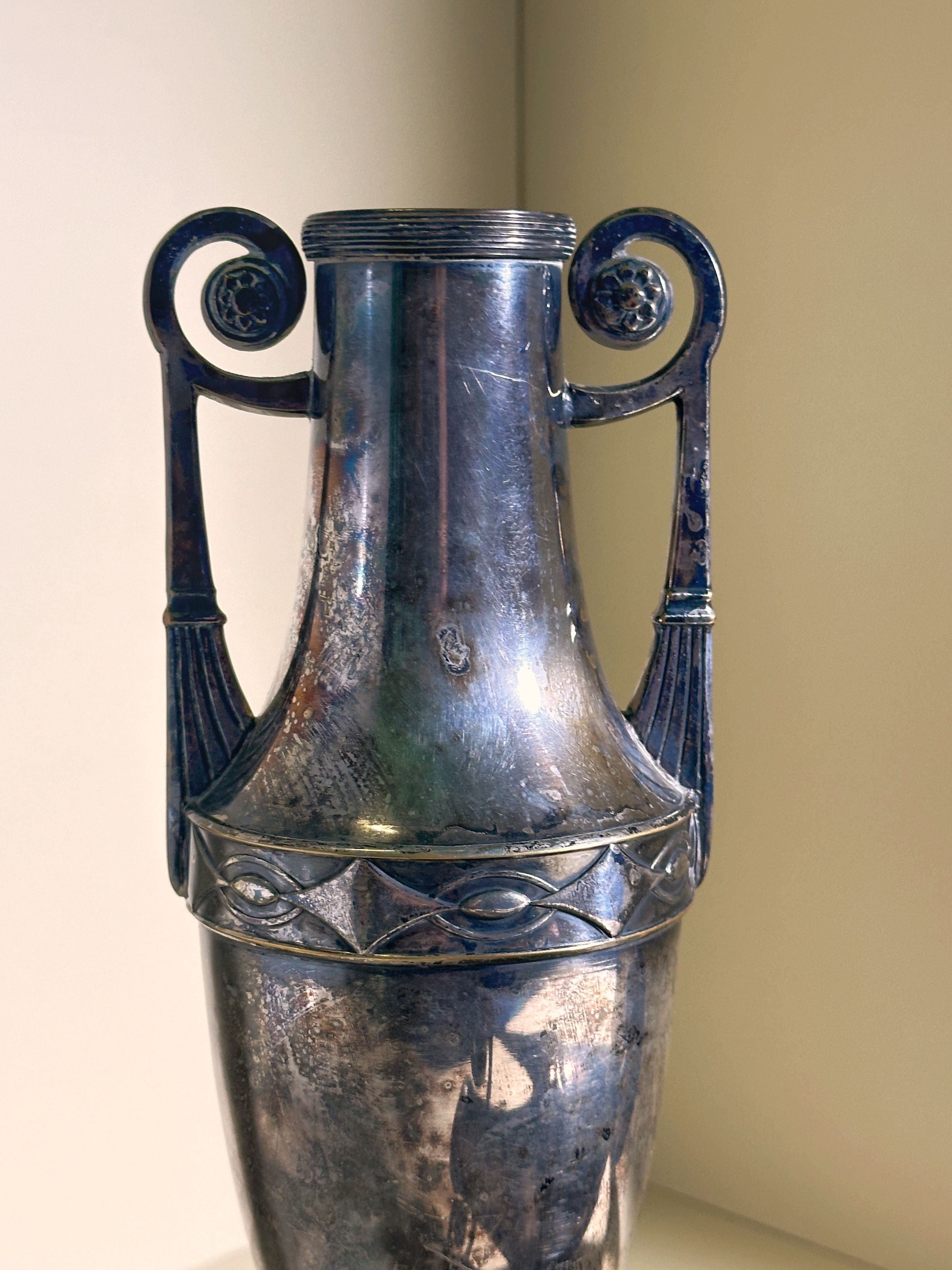 The Dodo Vintage Pair of Silver-plated Art Nouveau Amphora (1890) features a tall design with intricate spiral handles and decorative rim patterns, displayed against a plain background.