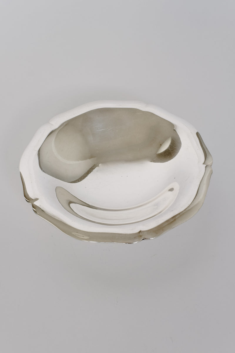 The Silverplated Bowl by septembre studios, with its shiny, round design and slightly wavy rim, exudes vintage appeal as it reflects light off its smooth surface against a plain white background.