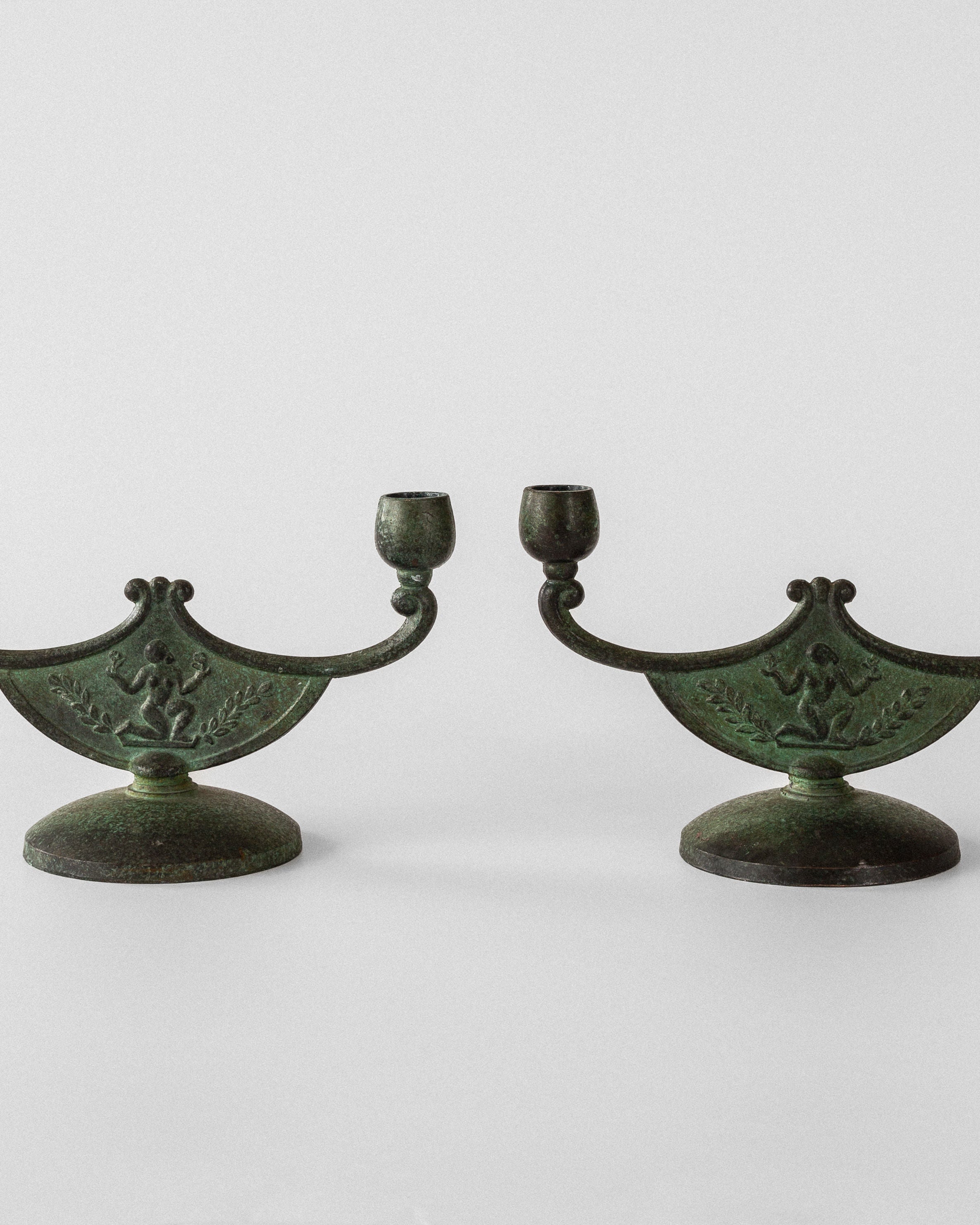 A pair of vintage Art Deco bronze candleholders by Spigel, featuring ornate leaf and bird motifs with a greenish patina, round base, and curved arms against a plain white background exemplifying Swedish metalwork elegance.