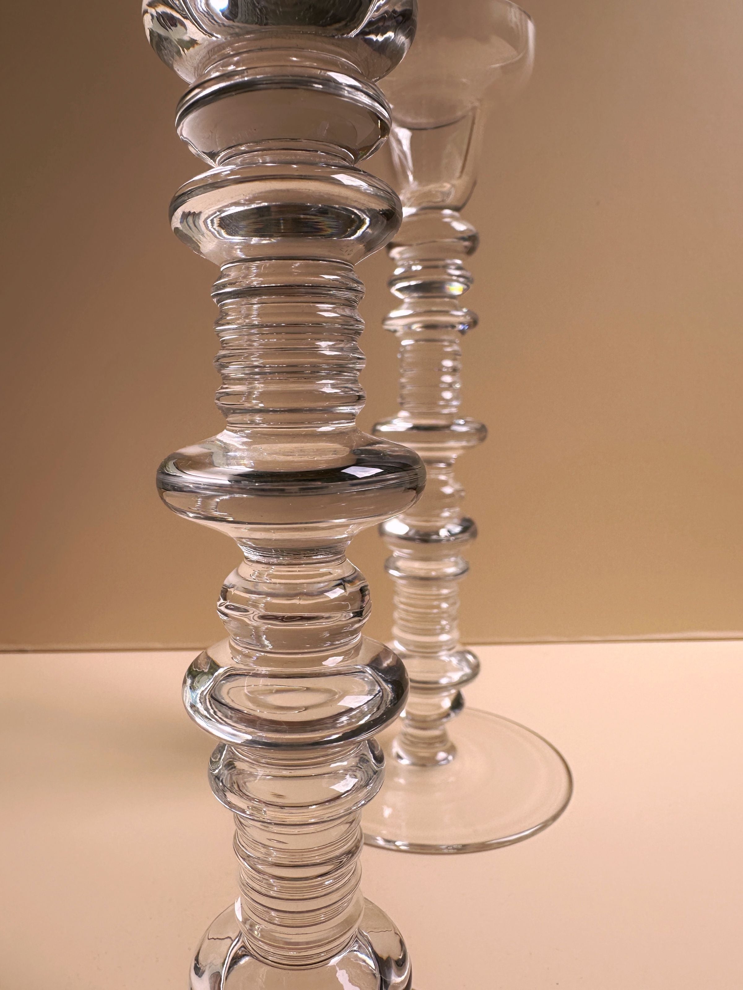 A close-up of a set of 2 glass candleholders by Peill & Putzler, offered by Dodo Vintage, showcases their intricate stacked ring designs that evoke mid-century elegance. Placed against a smooth, neutral background, their glossy finish beautifully reflects the light.