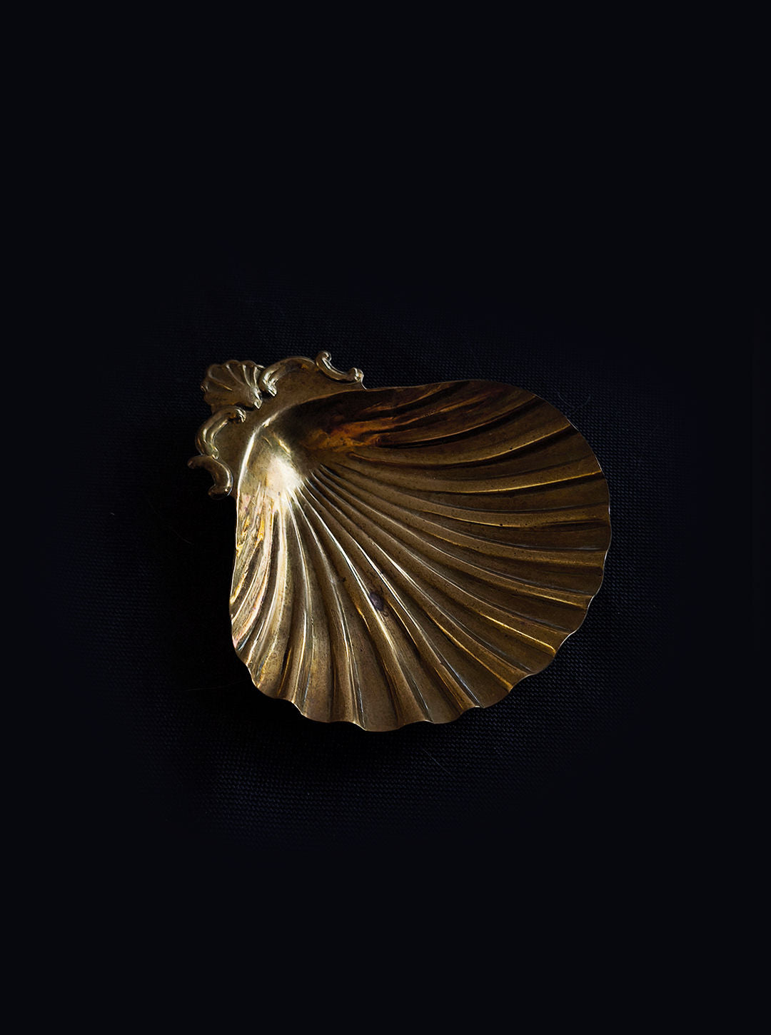 A brass Shell Brass Vide Poche by Les Objoies, shaped like a seashell with intricate detailing near the handle and curved ridges, is set against a dark background to echo the elegance of vintage design.