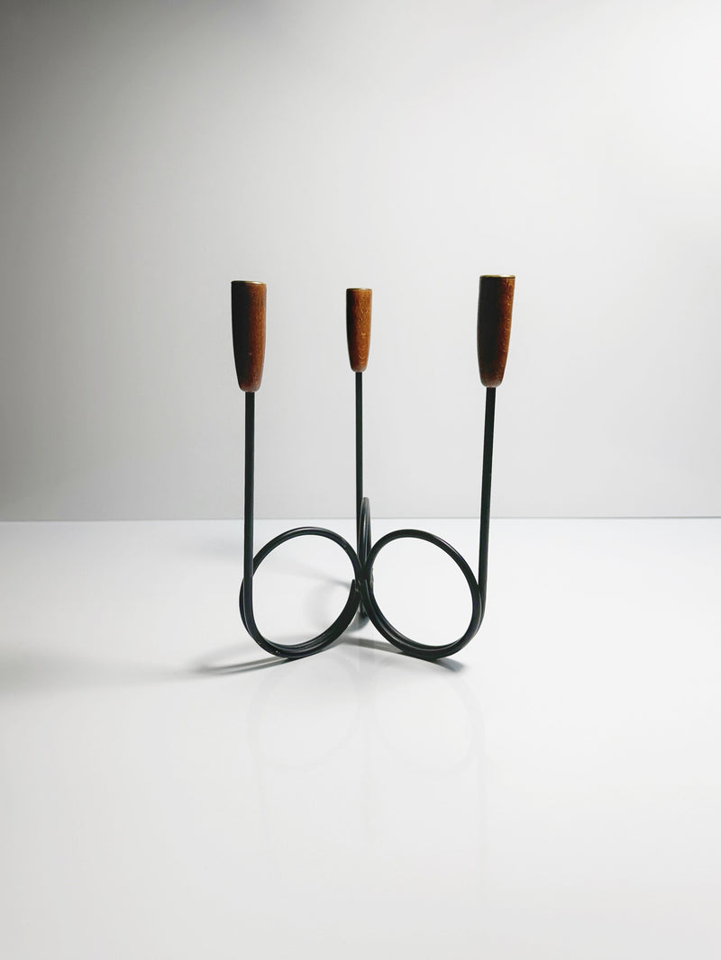 The Danish Candleholder 1960s by Dodo Vintage, a minimalist black wire candelabra with two circular bases and teak ends, designed by Lüthje Denmark, is placed on a reflective white surface with a plain light gray background.