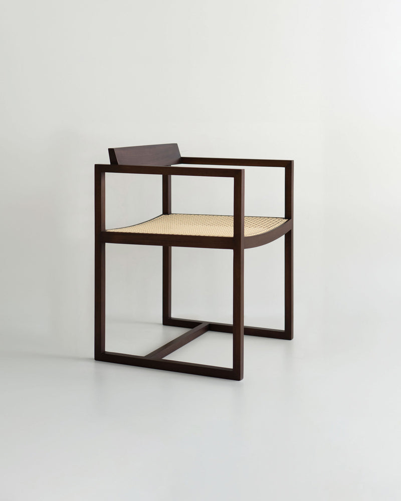 The "Amélia" Armchair by Andre Grippi features a minimalist design with a dark wooden frame, square armrests, and a woven straw seat, set against a plain light background.