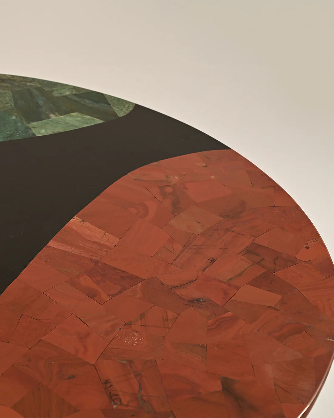 Close-up of the LMNOH Jasper Coffee Table displaying a mosaic tabletop design. It features an irregular pattern with red-brown and dark green semi-precious stones, boasting a smooth, glossy finish that enhances the stunning color contrast.