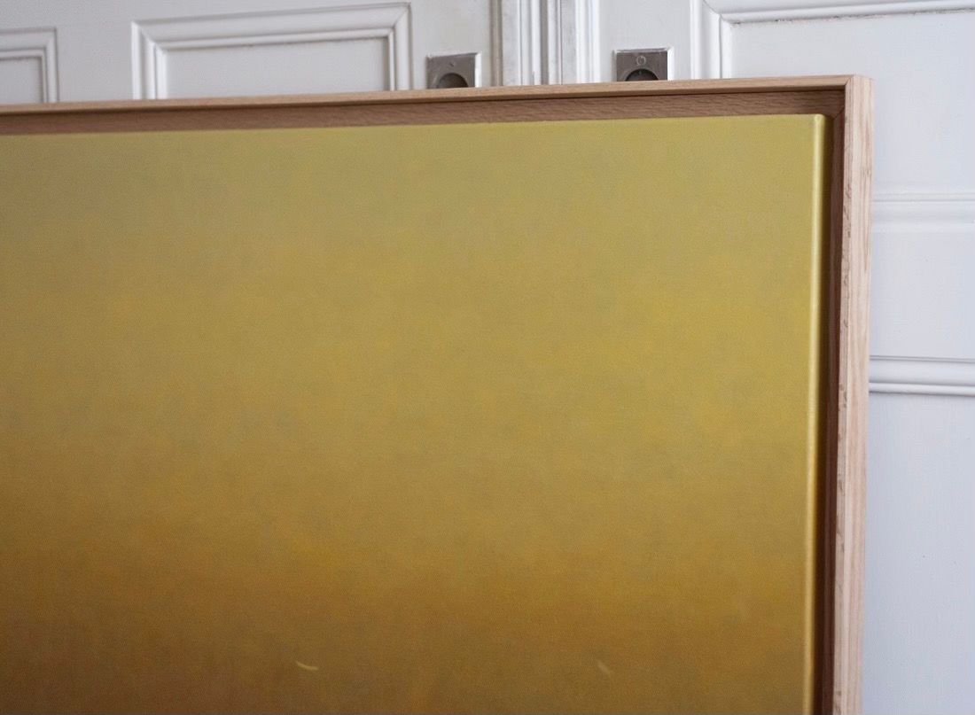 The 'Morning Hue' Painting by Rebecca von Matérn, featuring a smooth yellow to beige gradient, is elegantly framed in hard waxed oak and leans gracefully against the white paneled door.