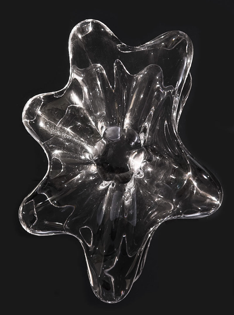 The Les Objoies Crystal Baccarat Cup features an abstract glass design with wavy edges and a hollow center in a star or flower shape. Set against a black backdrop, it reflects light brilliantly, resembling a modern vessel and epitomizing crystal artistry.
