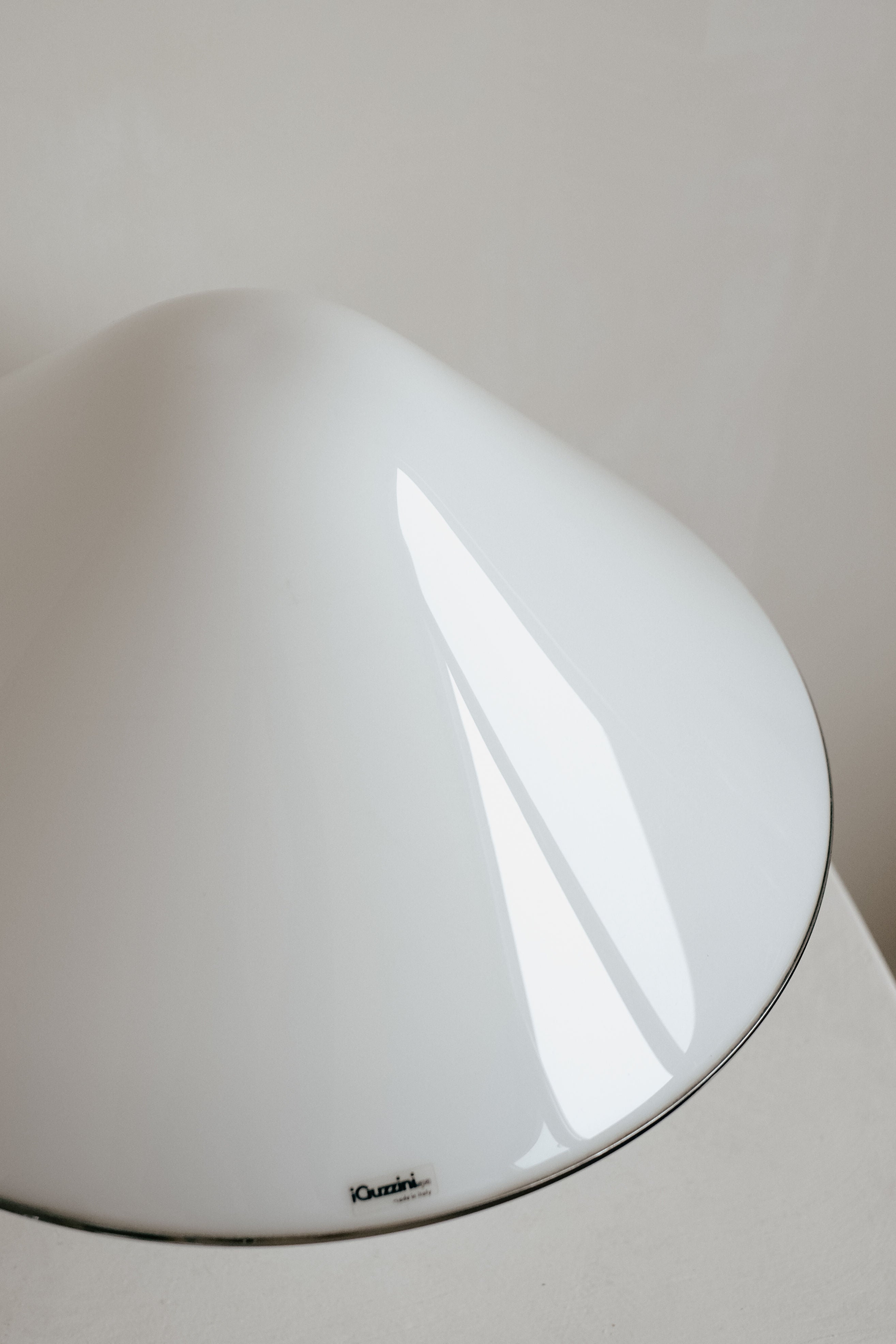 A close-up of a sleek, white, dome-shaped lampshade from the septembre studios Harvey Guzzini Elpis Table Lamp collection. Its glossy finish casts subtle shadows on its smooth curves, and a small, indistinct logo is visible near the edge of this Luigi Massoni design.