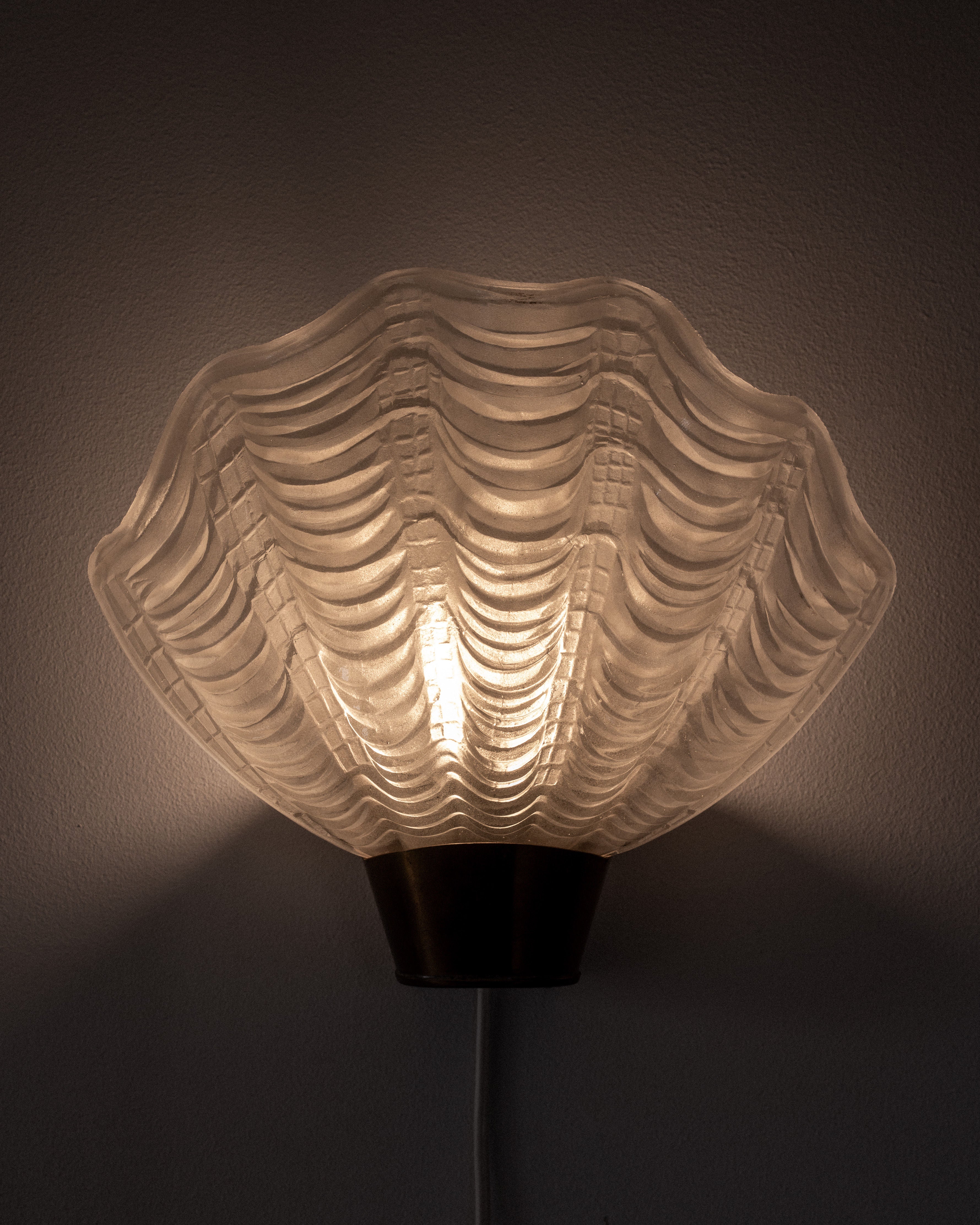 The Vintage "Coquille" Wall Light by Spigel is a 1940s Swedish design that softly illuminates beige walls with its scallop-shaped form. Its layered glass pattern exudes a cozy ambiance, perfectly blending Art Deco style with modern elegance.