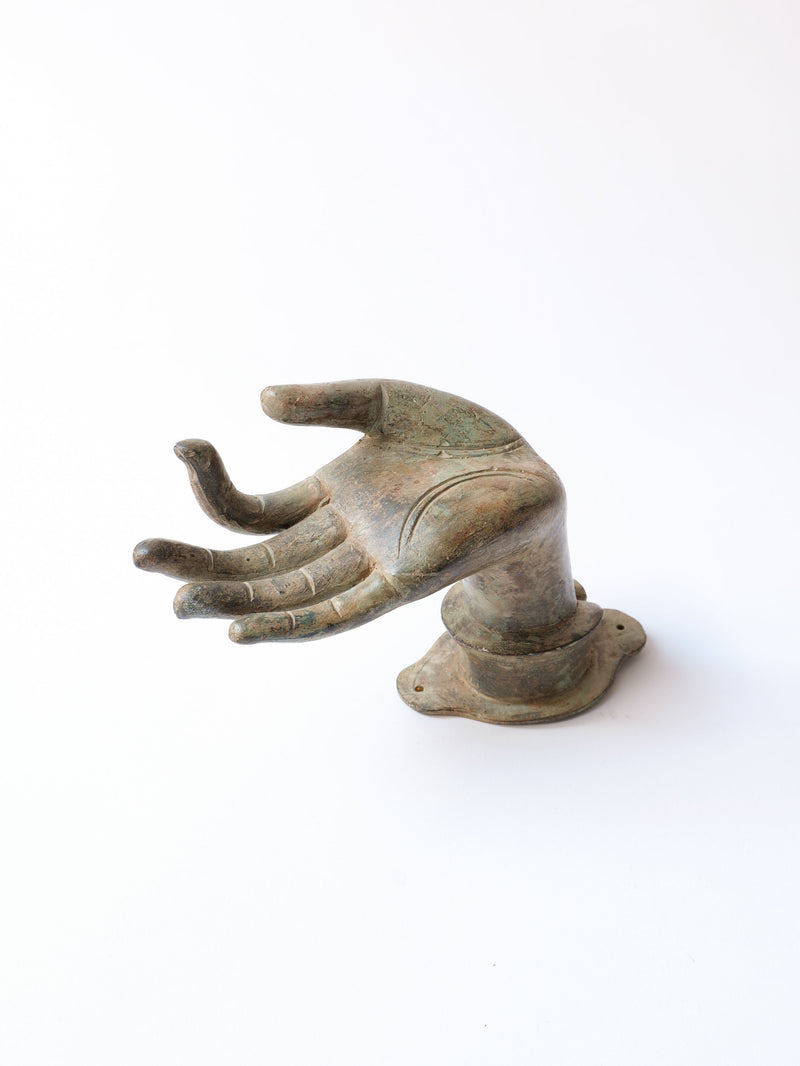 Ancient bronze sculpture of a right hand, fingers slightly curled, and palm facing upwards. This elegant bronze piece has a weathered, greenish-brown patina and is mounted on a small base. The Bronze Hand by Collection apart emanates emotional power against the white, seamless background.