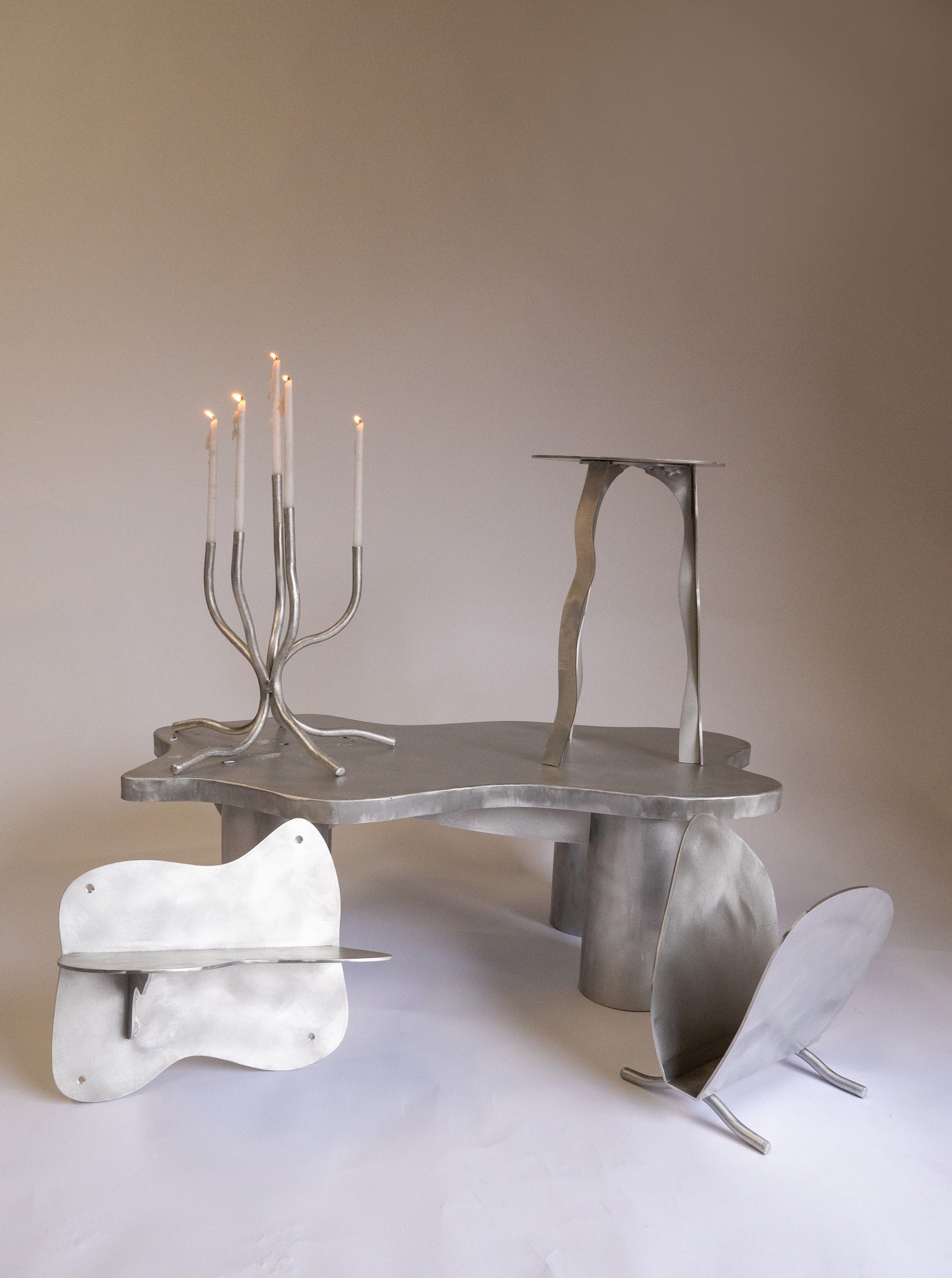 A surreal, metallic furniture set containing a table, chair, and Six Dots Design Small Candelabra with curved and irregular shapes, set against a neutral backdrop.