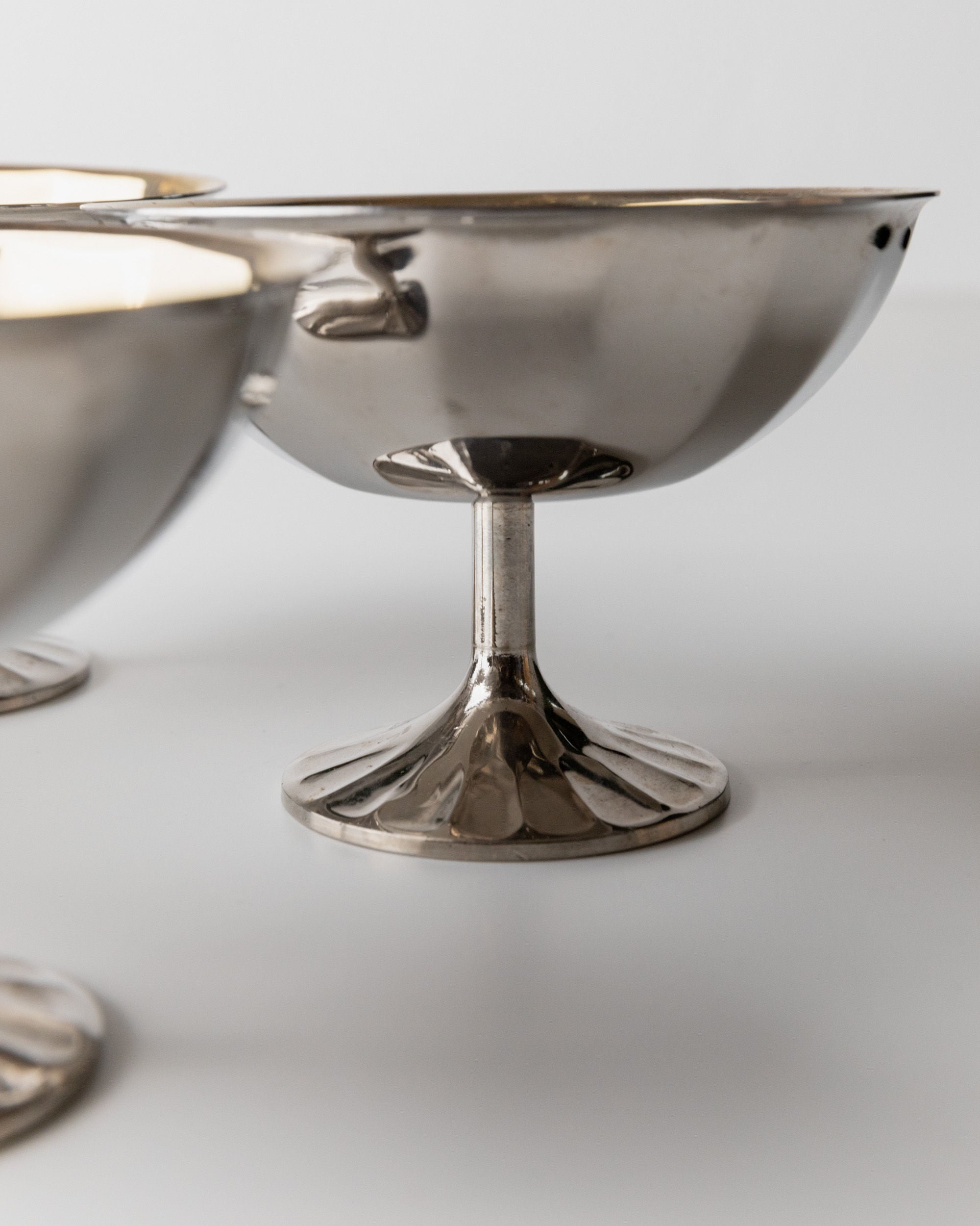 Close-up of elegant Bottega Jacobs Champagne Coupe, Italy 1970s, with a reflective surface on a sleek white background. The fluted stems and polished, shiny shallow bowls capture the charm of vintage champagne bowls.