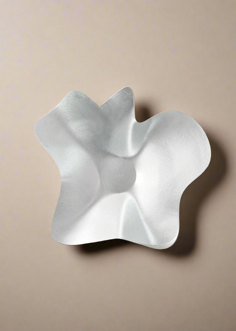 Crafted by Six Dots Design in their North London Workshop, the Mid Bowl features a modern, abstract design with a wavy, irregular form. Its silver metallic finish reflects light and shadow beautifully, adding dynamic visual interest against a plain backdrop.