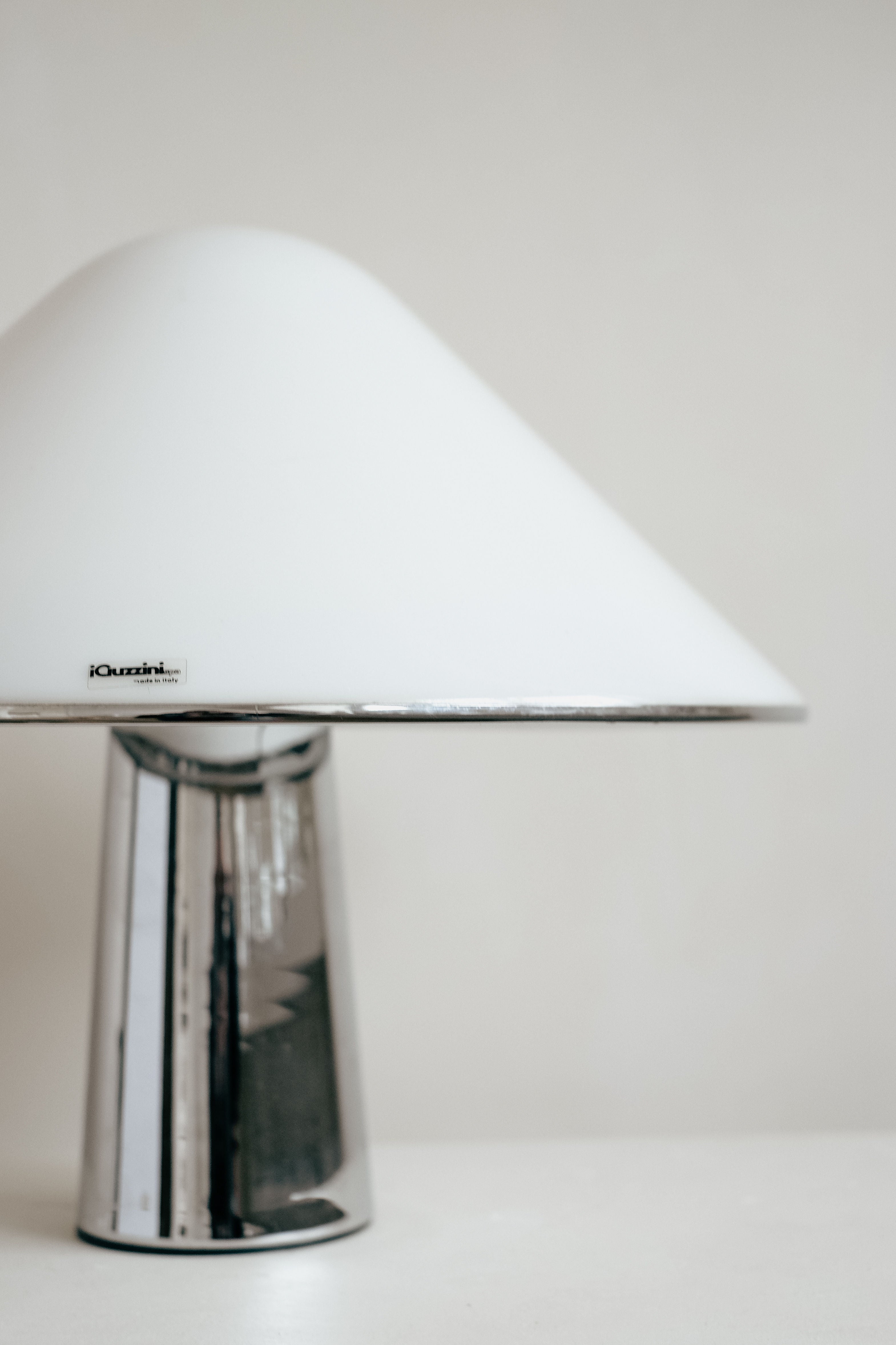 Explore the elegance of the Harvey Guzzini Elpis Table Lamp by septembre studios, featuring a shiny metallic base and large smooth white conical shade. Inspired by Luigi Massoni, its minimalist charm shines against a plain background, retaining its vintage condition.