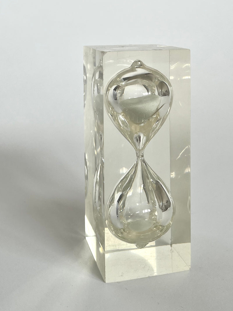 A transparent lucite cube encases the elegant Hourglass by Charles Hollis Jones, 1970s, designed by septembre studios. The hourglass inside is a clear, fluid form, suspended within the solid block against a plain white background.