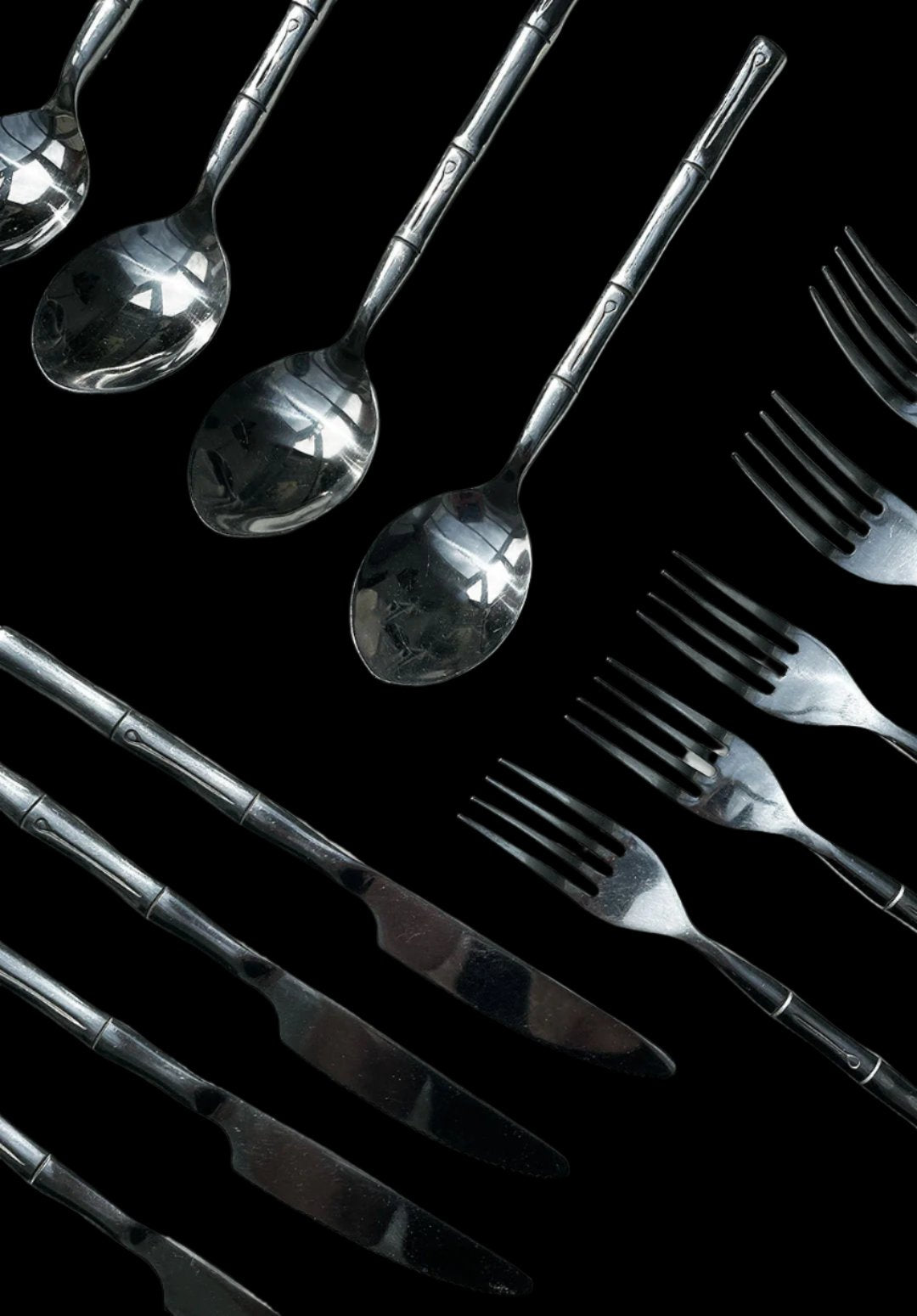 A black background with an array of Les Objoies' bamboo utensils neatly arranged, including three spoons at the top, five forks on the right, and four knives on the left. The bamboo cutlery features a mildly reflective surface with a simple, yet elegant design on the handles.