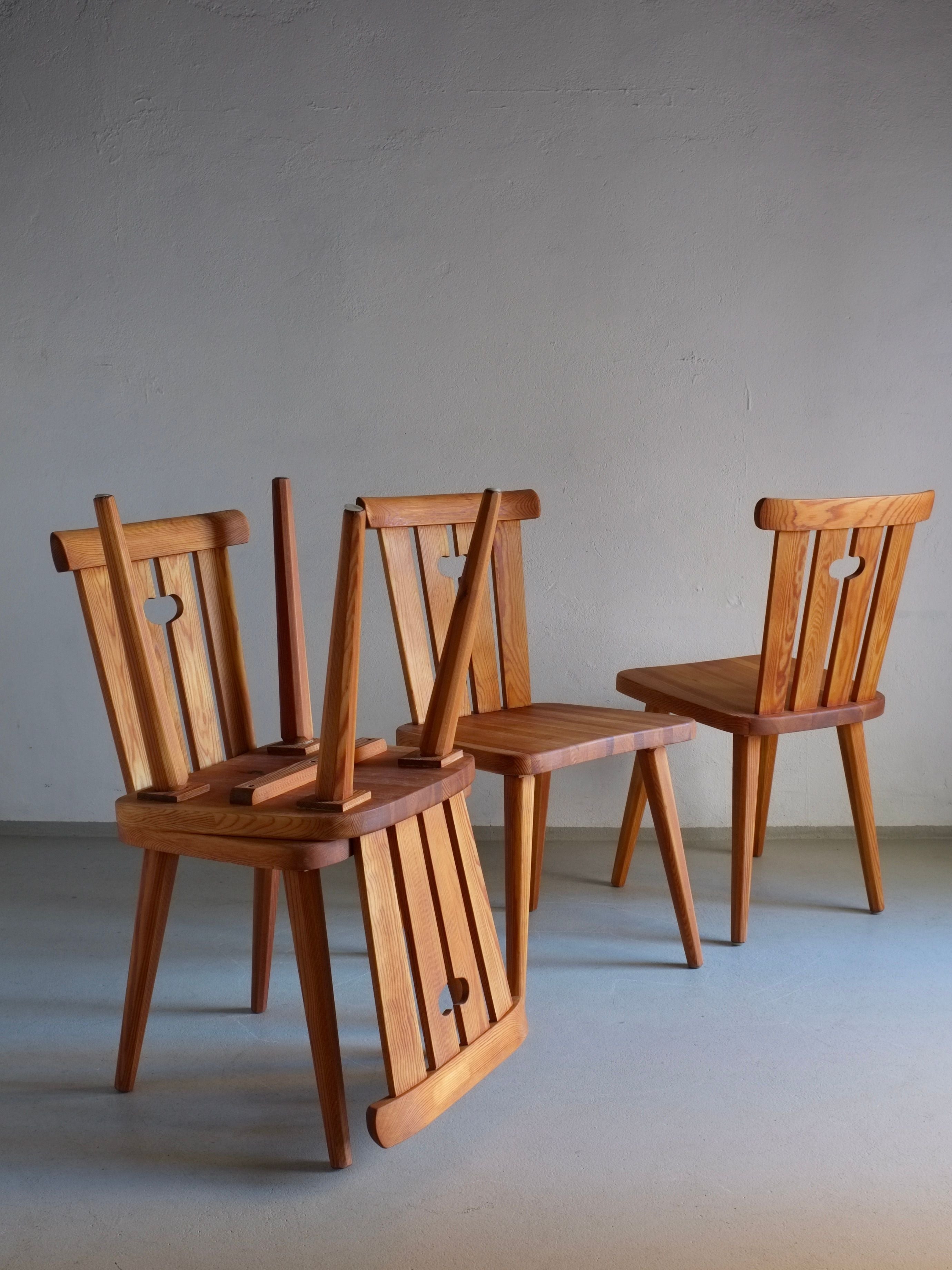 Four rustic pine chairs by Göran Malmvall, crafted in Sweden during the 1940s and offered by Veter Vintage, feature restored and oiled finishes with decorative cut-outs in the backrest. They are arranged on a light-colored floor against a plain, light gray wall, exemplifying Malmvall's simple and elegant design with warm-toned wood.