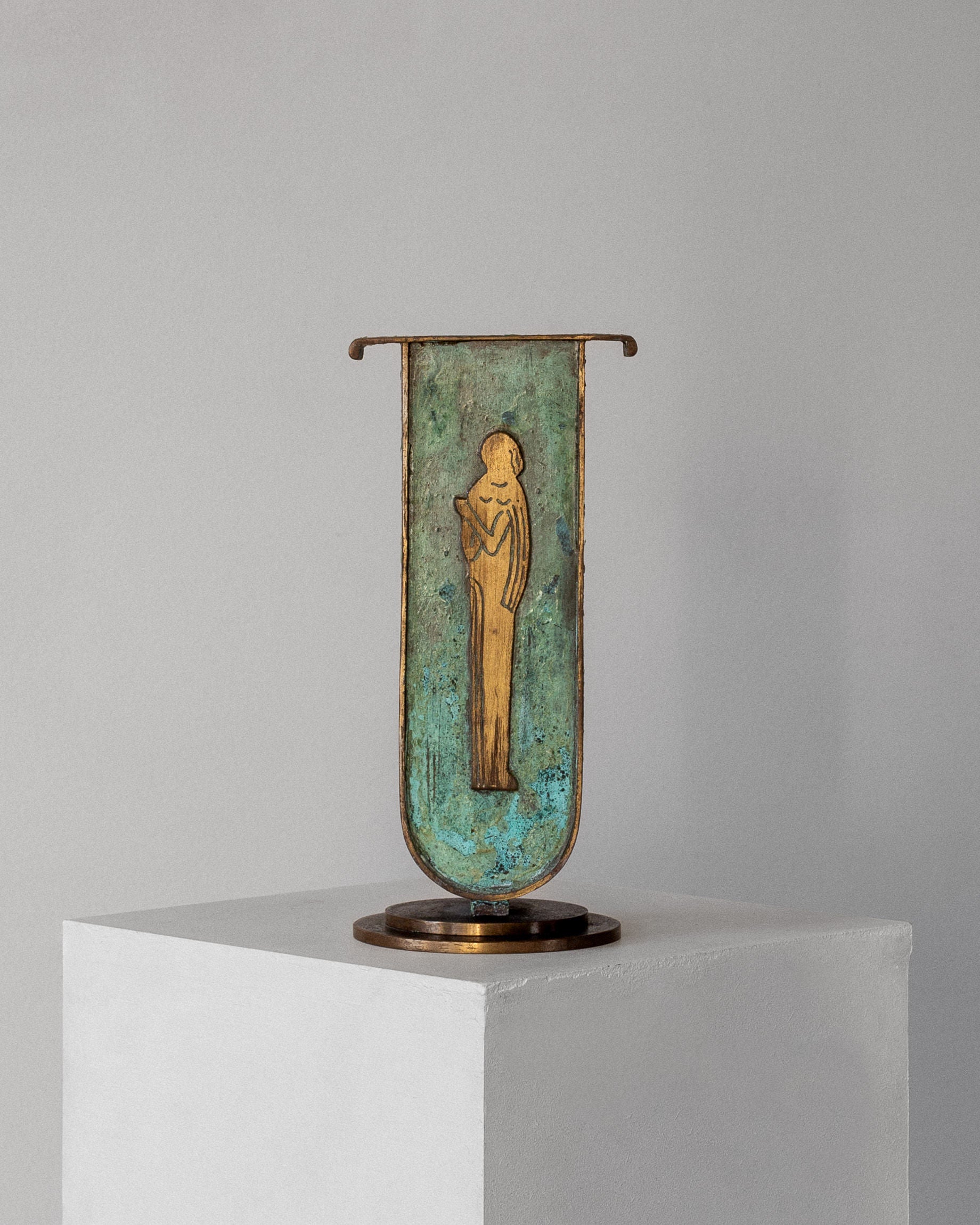 The Spigel Art Deco Brass Vase with Verdigris Patina showcases an abstract style on a square white pedestal against a grey background. Its elongated form and stylized features contribute to its modern artistic allure.