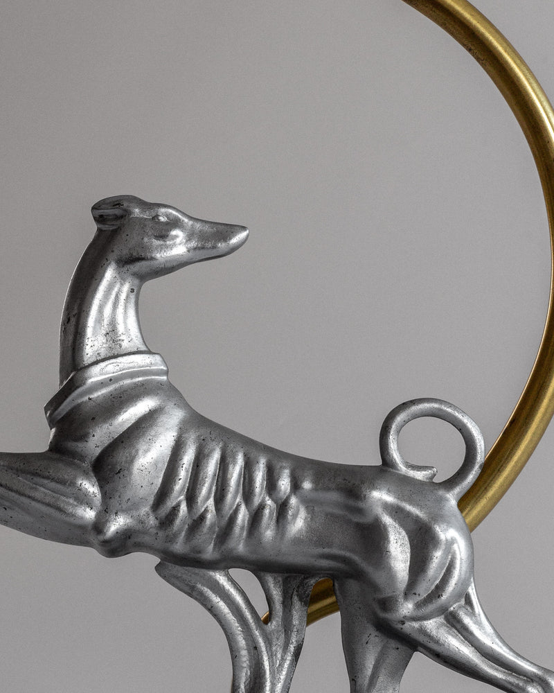 A close-up of the Spigel Art Deco Greyhound Table Lamp, 1930s, shows its metallic, streamlined body framed by a gold circle, echoing the iconic design from the Stjärnmetall collection.