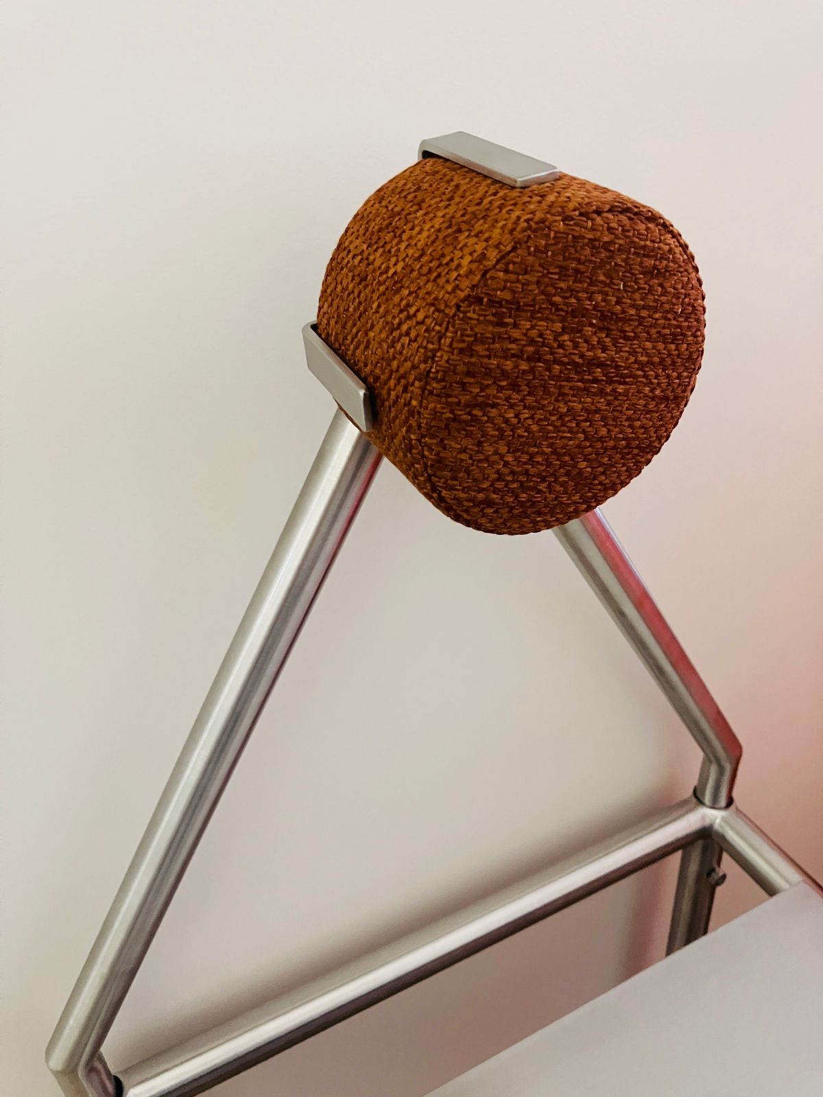 A close-up of the HT. 'H01' Stainless Steel Chair, showcasing its modern design with a triangular backrest and a removable brown textured cushion secured by two metal brackets at the top.