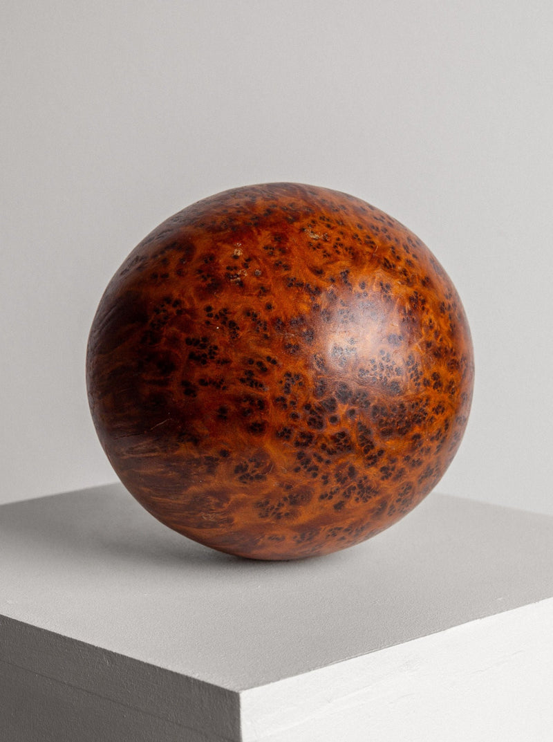 The Vintage Burl Wood Spherical Ball Sculpture by Spigel, featuring a polished, spherical form with a reddish-brown, mottled Thuya burl wood surface, rests elegantly atop a white pedestal against a plain gray background. This stunning handcrafted piece serves as both a sculpture and an exquisite decorative accent.