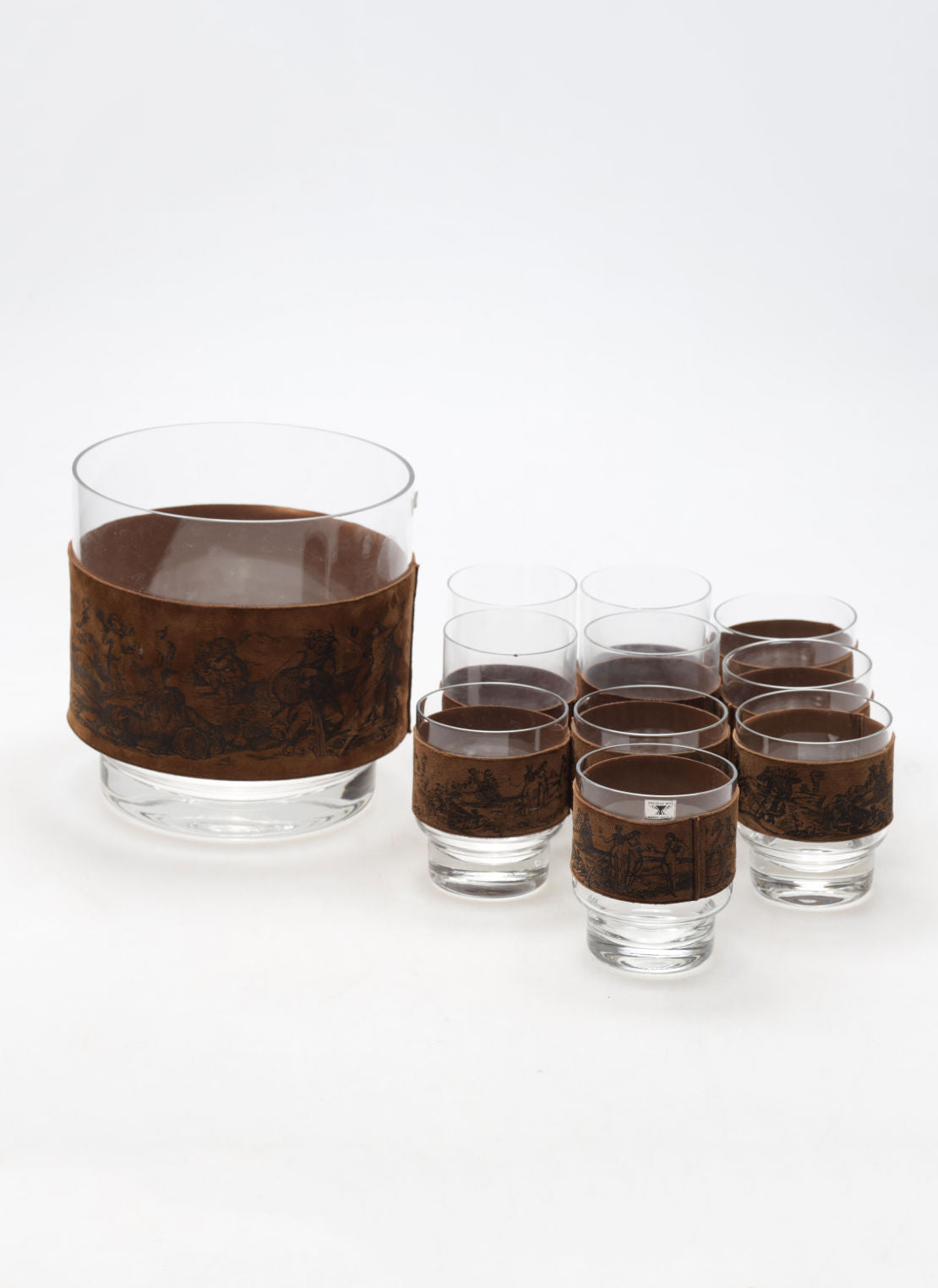 The Ice Bucket and Glasses by Edelglas Wien, c. 1960 from RELIC LONDON features a large glass bowl with seven smaller glasses, each with a brown etched pattern. Perfect for any occasion, these beautifully crafted pieces are showcased against a plain white background.