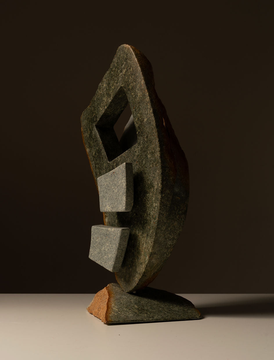 The Two-toned Abstract Sculpture by Les Objets Amsterdam is a handmade art piece crafted from natural stone, featuring geometric shapes with a vertical, leaf-like form, a square cutout at the top, and two rectangular blocks below—all set on a flat base against a dark background.