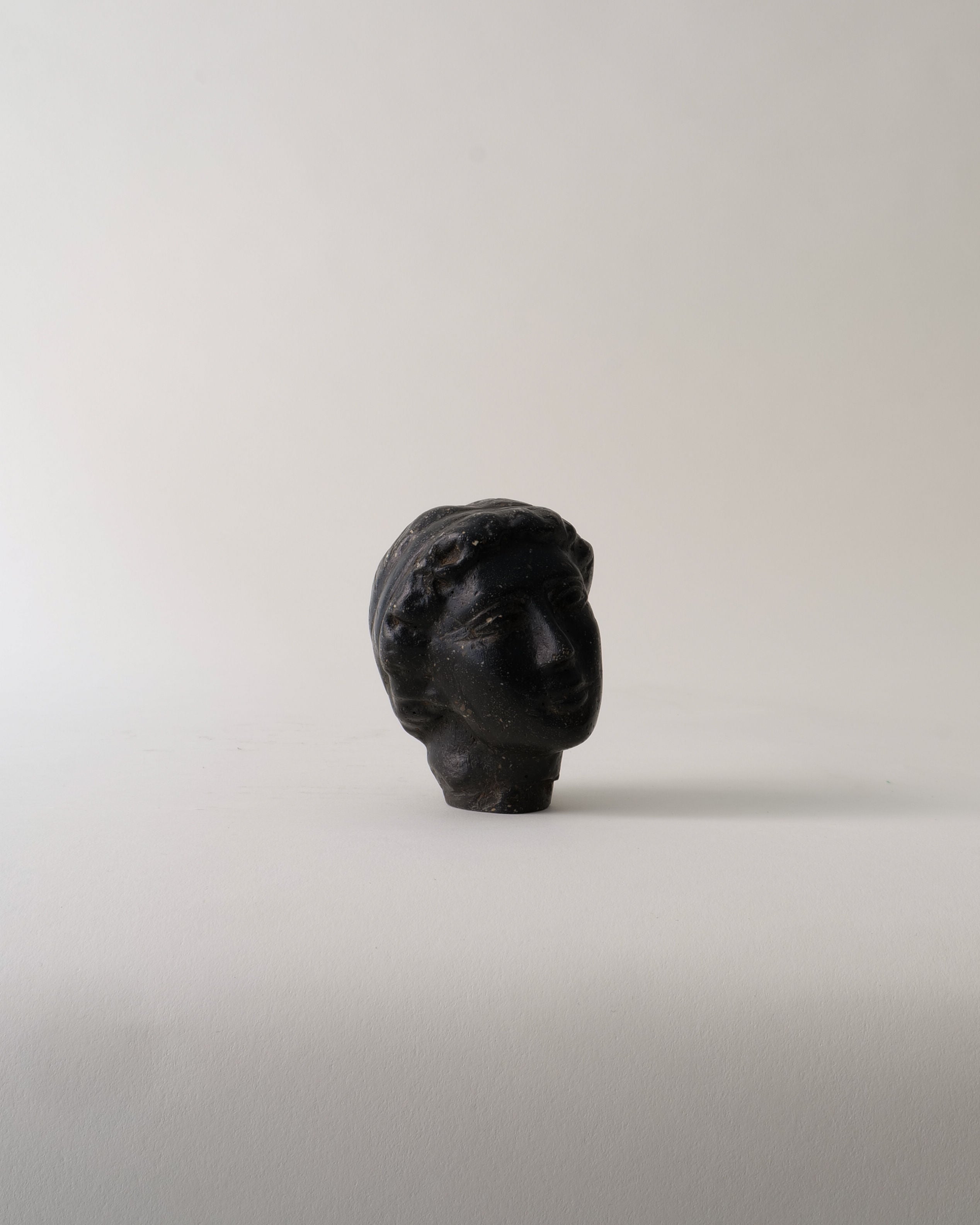 The Venus Stone Sculpture by Collection apart is a compact, dark stone composite bust of a classical head with short, wavy hair, set against a light background. Its ancient, weathered look captures the timeless elegance of Venus.