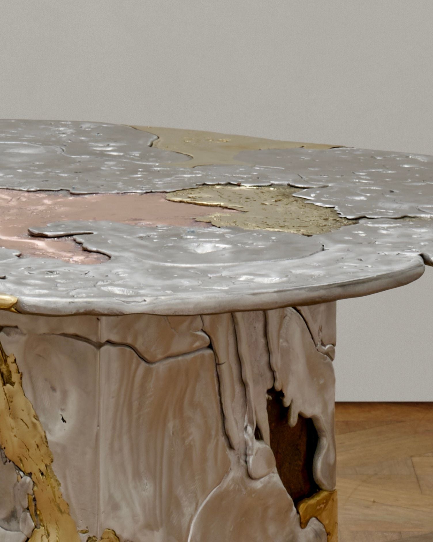 A close-up of the 'Elemental Patchwork' Coffee Table by Sheyang Li, showcasing its uneven, molten metal surface in silver, gold, and pink hues with a textured, melted look and organic edges.
