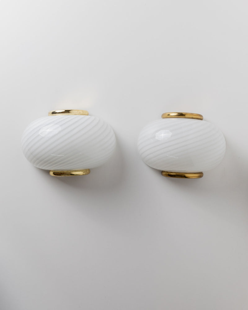 Two Murano glass wall lamps by Bottega Jacobs, featuring a white background with classic swirl patterns and subtle diagonal stripes accented in golden metallic.