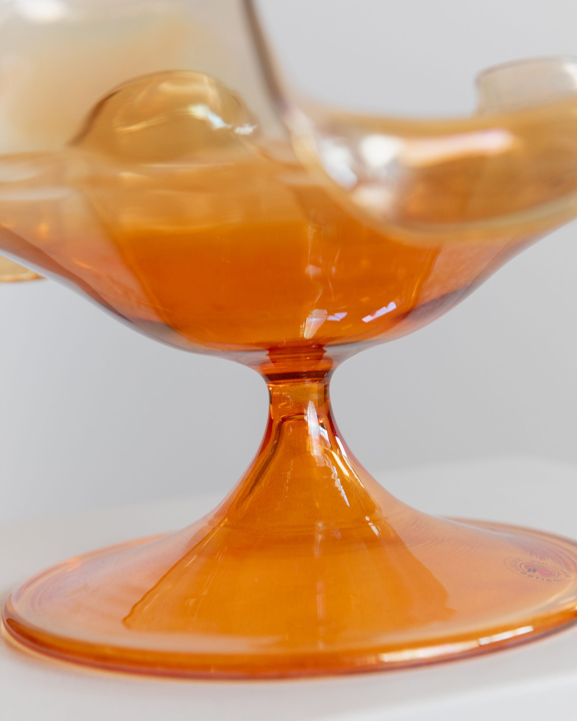 Close-up of a Murano Glass Bowl by Parise Vetro 70s from Bottega Jacobs, featuring an orange iridescent finish with a smooth, wavy design, set against a neutral background. The base is slightly elevated, showcasing its elegant, curved shape—an ideal decorative piece for any setting.