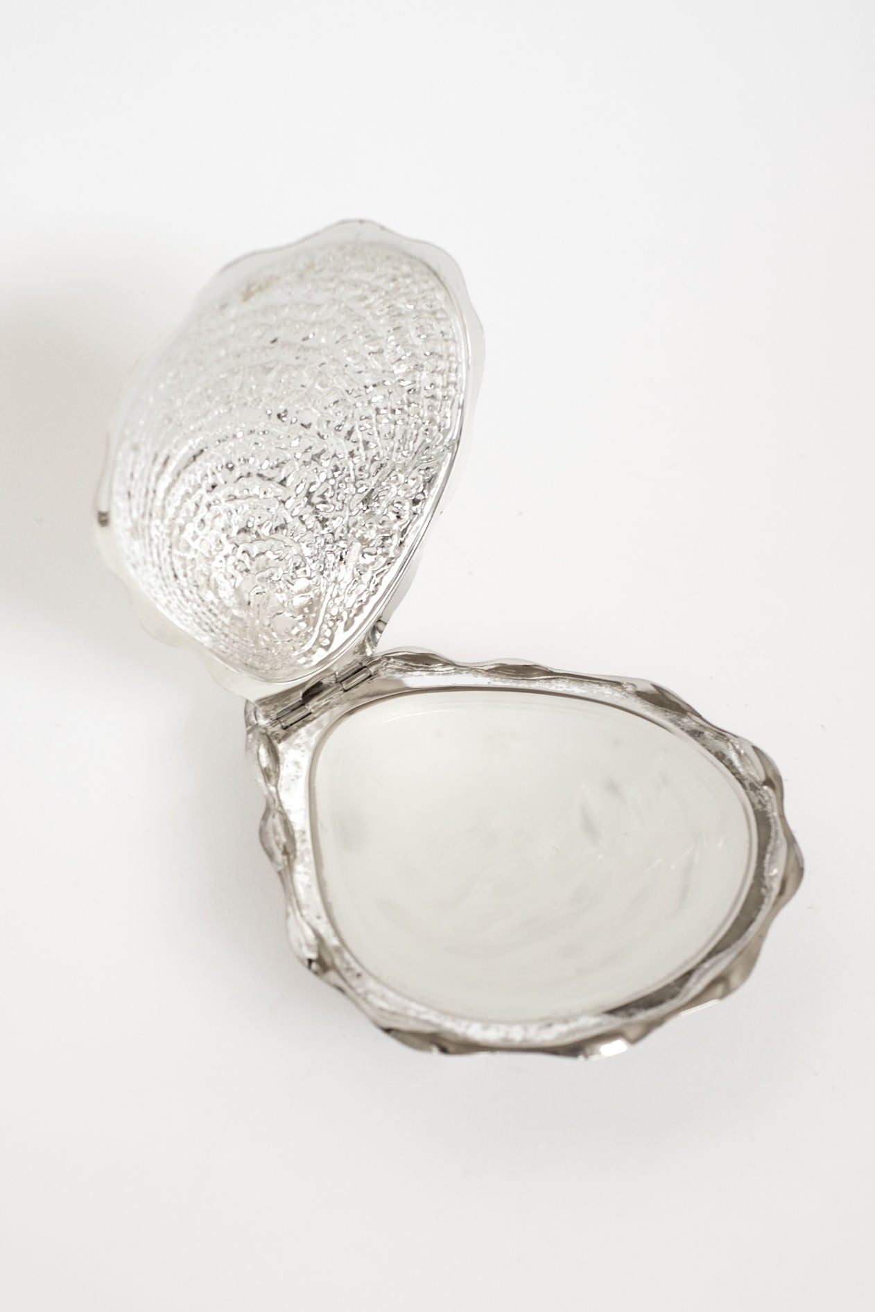 The Shell Butter Dish by septembre studios is an open, silver, scallop shell-shaped case with a textured exterior and smooth, shiny interior, displayed against a white background.