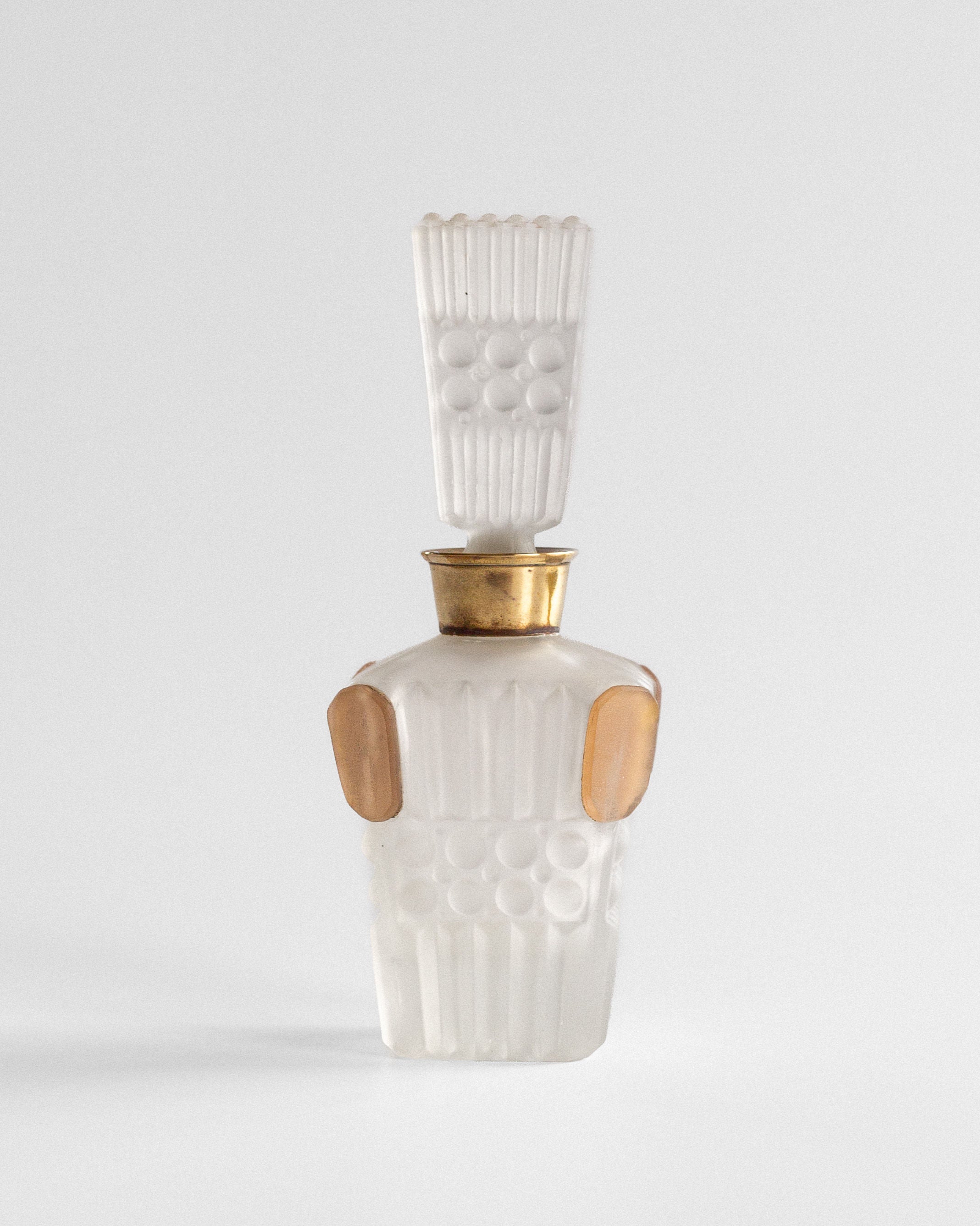 The Spigel Art Deco Perfume Bottle from 1930s France features a decorative vintage design with a tall textured stopper. Its frosted translucent glass with gold accents showcases raised circular and vertical lines in an ornate, symmetrical pattern.