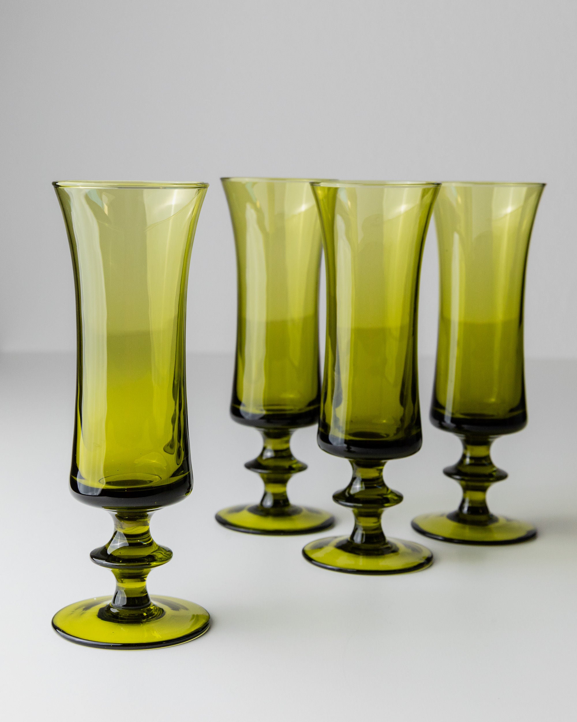 The 4 Murano Glasses in Green 70s by Bottega Jacobs are displayed on a light surface with a neutral backdrop, featuring wide bases and tapered bodies for a retro chic vibe.