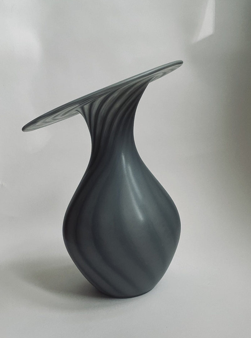 A contemporary sculpture with a twisted, vase-like form and an asymmetric, flat top boasts a high-quality glass surface similar to the Vintage Vase Peill & Puztler by Flock Studio. It features delicate swirling patterns on a plain white background that evoke classic Peill & Putzler designs.