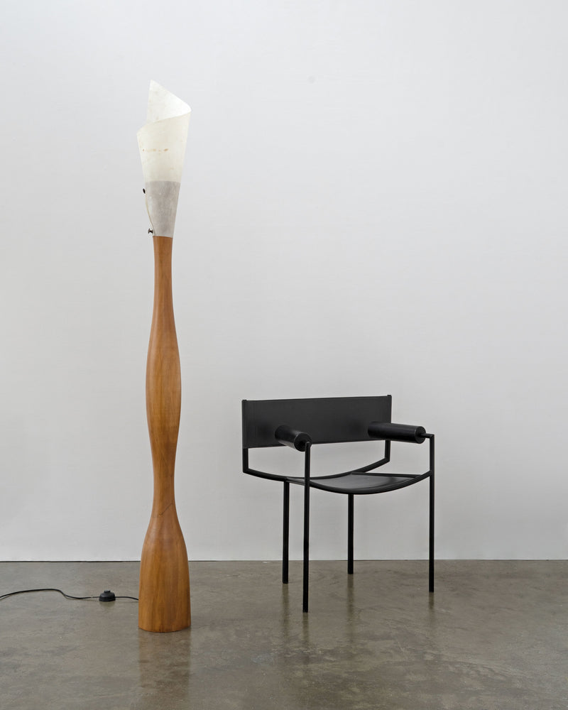 Wooden sculptural floor lamp with white shade next to black chair