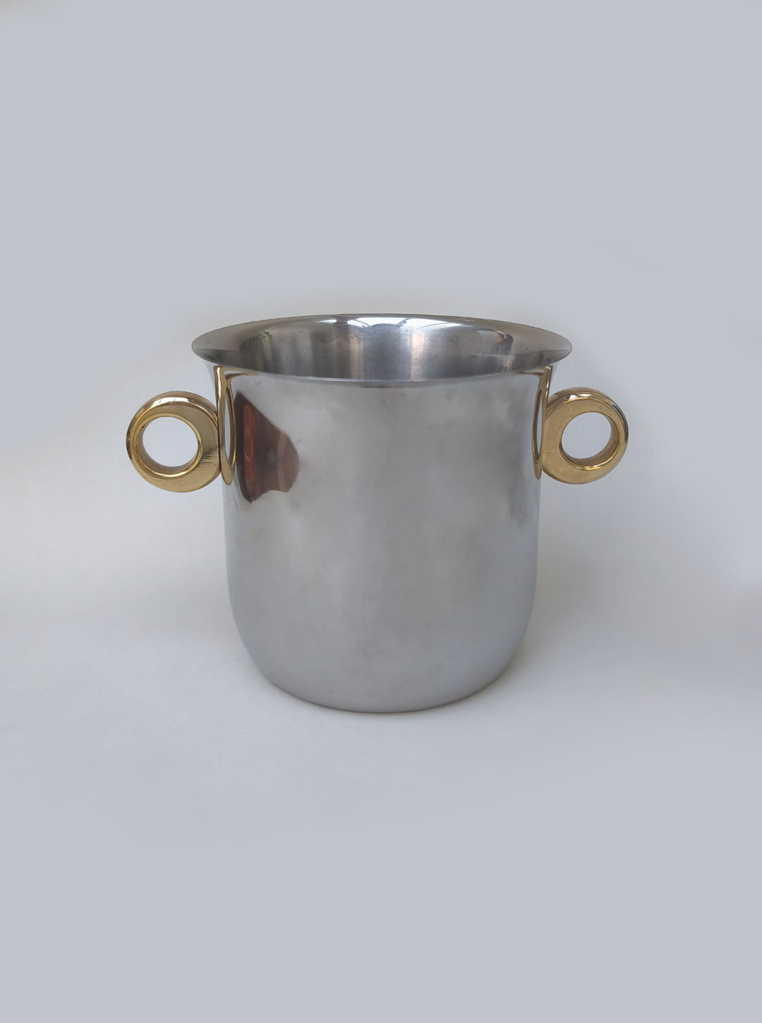 The Les Objoies "Ice Bucket, Italy 1970s" features shiny stainless steel and two large round brass ring handles, shown against a plain light gray background.