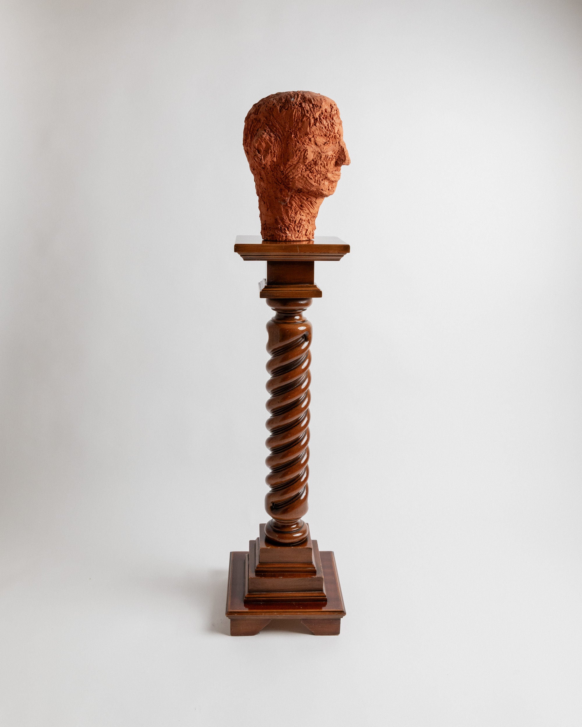 A terracotta bust is showcased on a vintage Bottega Jacobs wooden stand from Italy in the 1960s, featuring a spiral design, set against a plain background.