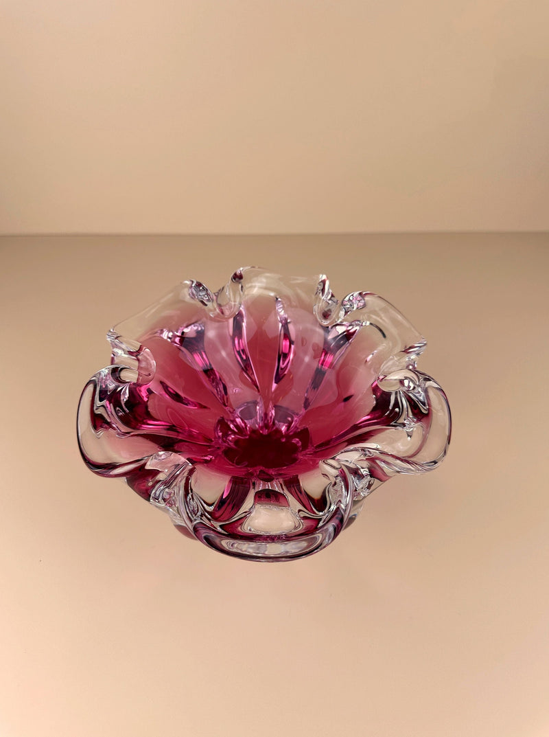 A pink Bohemian Cranberry Red bowl by Josef Hospodka with delicate, translucent petals, crafted by Bohemian glassmakers and displayed against a soft, off-white background. The bowl's design mimics a blooming flower with
